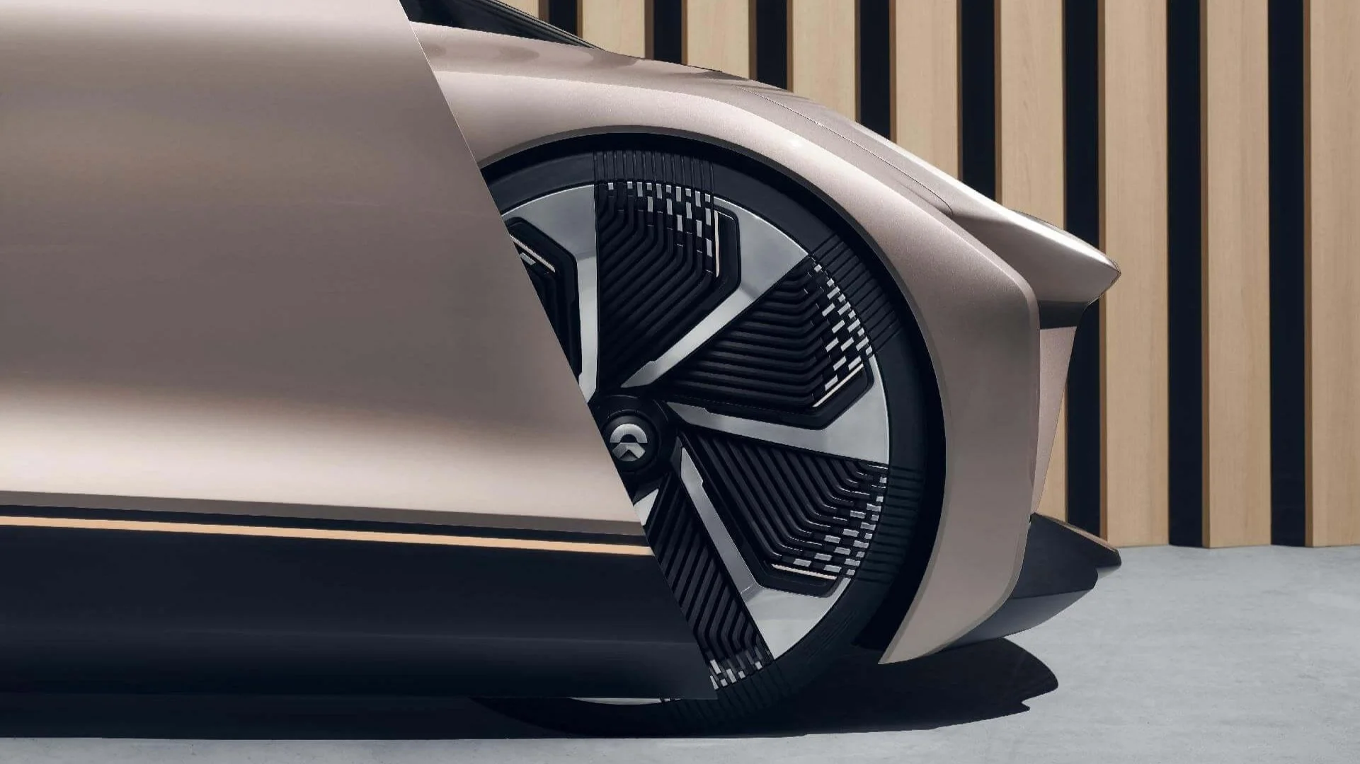 Nahaufnahme eines futuristischen Autoreifens mit einem modernen Design und silberner Karosserie vor einer Wand aus Holzlatten.