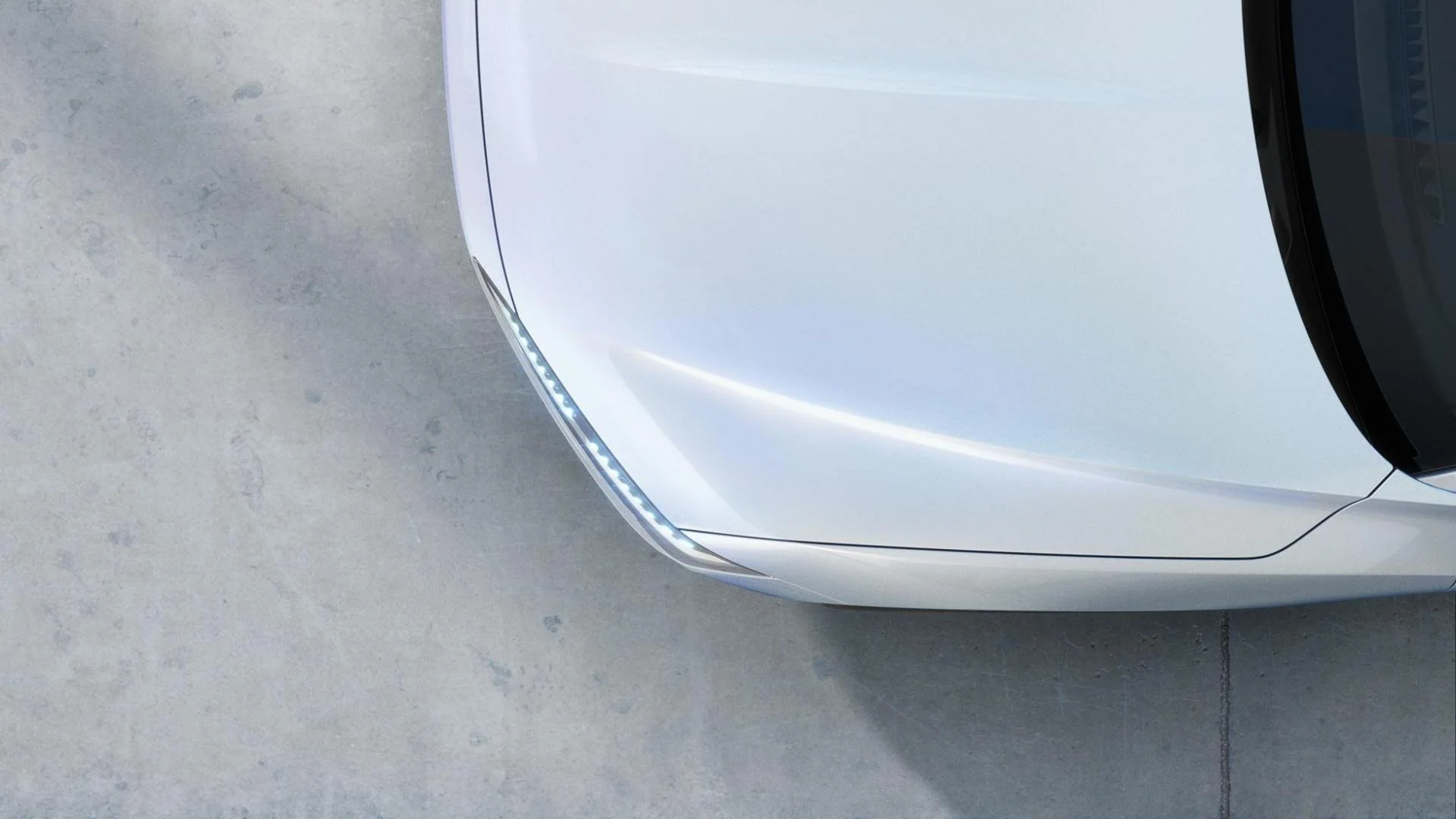 Nahaufnahme der vorderen rechten Ecke eines weißen Elektroautos mit LED-Scheinwerfern, auf einer Betonbodenfläche.