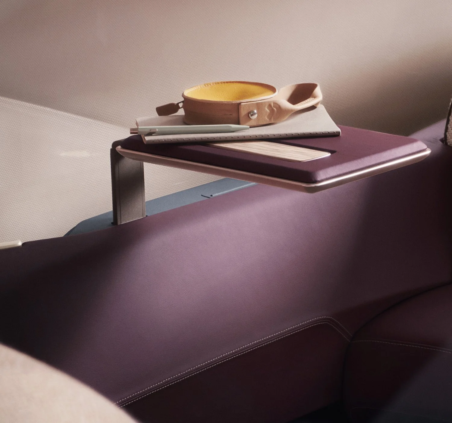 Ein Flugzeugsitz mit einer Ablage, darauf befinden sich eine Brille, ein Notizbuch, ein Kugelschreiber und ein Tablet.