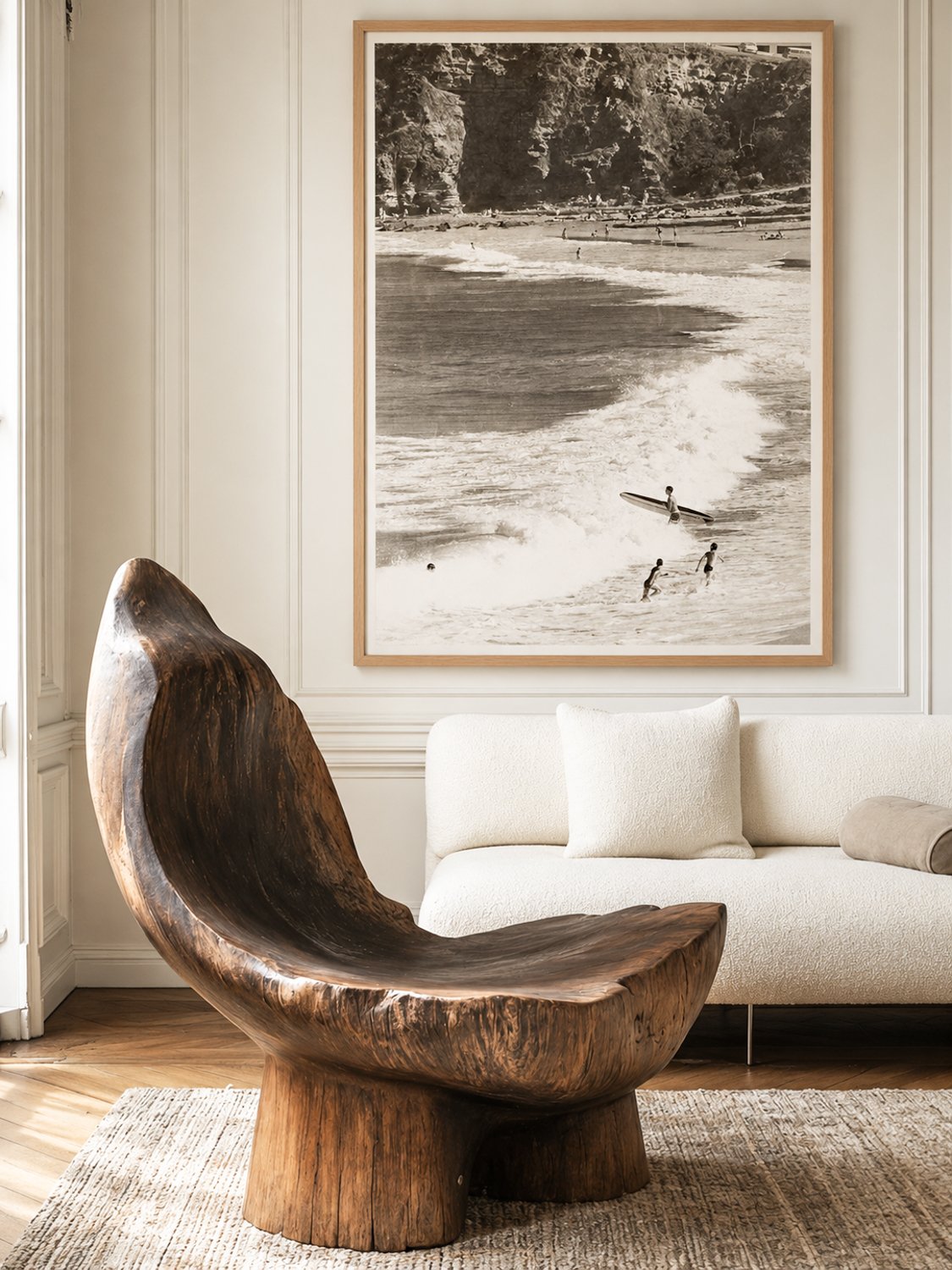 A living room with a wooden modern chair, a white sofa, and a large beach-themed black-and-white photograph hanging on the wall.