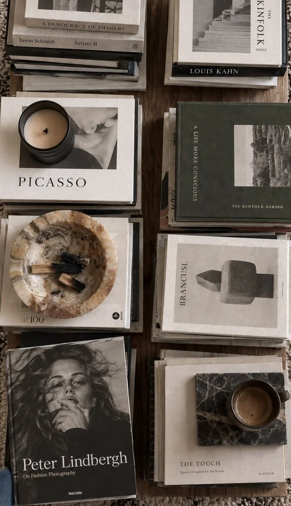 Books about art, photography, and design arranged on a table, with candles and coffee cups placed among them.
