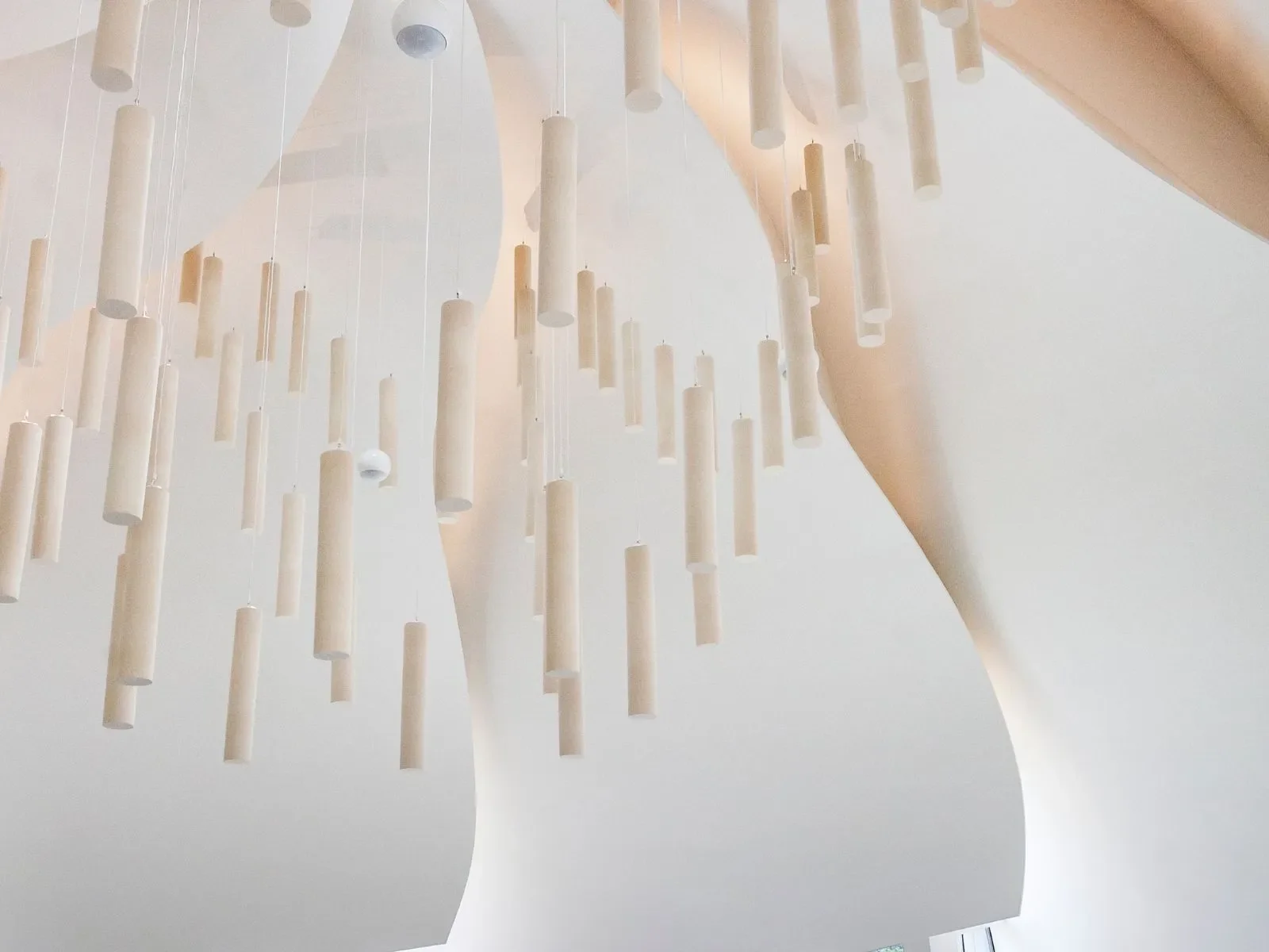 A modern chandelier with numerous white cylindrical pendants hanging at different lengths from the ceiling.