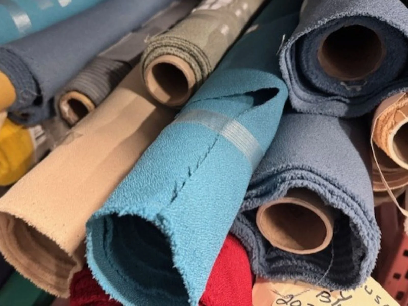 A collection of rolled fabric pieces in various colors including blue, gray, beige, and red, arranged closely together.