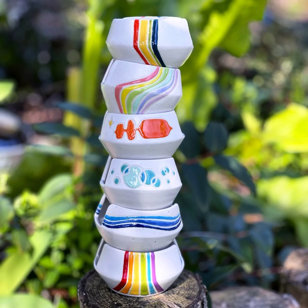 A stack of sponge holders all with a matte white finish and bright, colorful, unique, glossy designs.