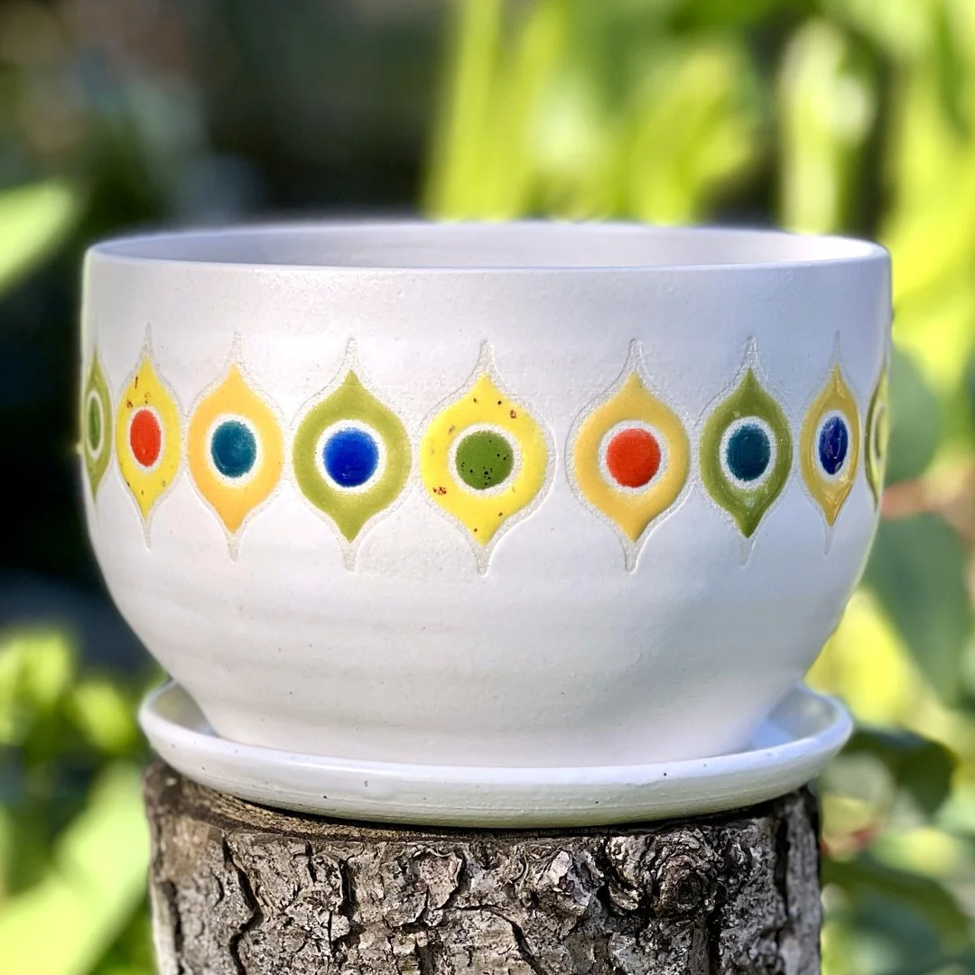 A large planter from Stuffed Studio's Retro Revival Collection featuring a matte white base with a glossy colorful mid century modern pattern in greens, yellows, oranges, and blues.