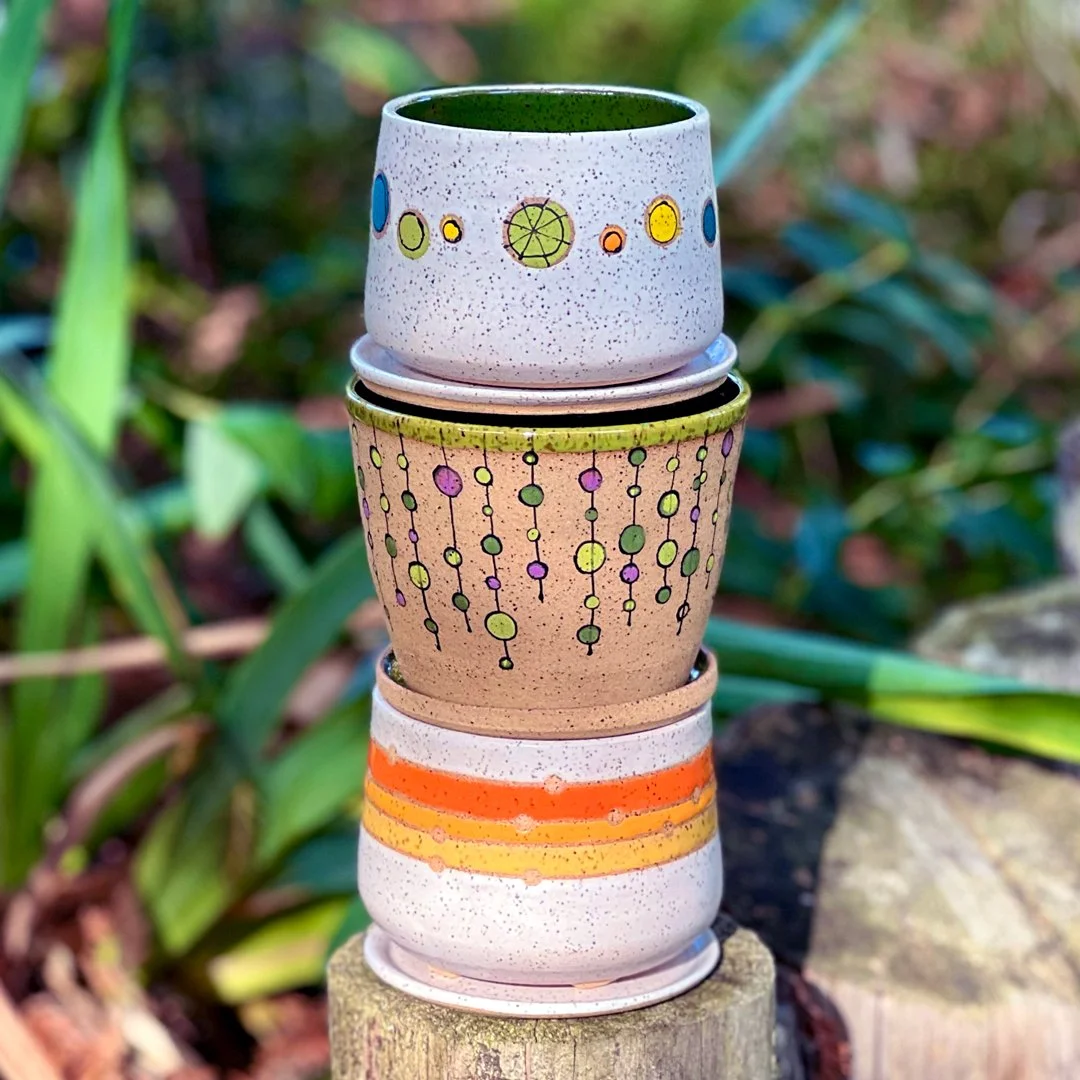 A stack of three small planters by Stuffed Studio. All with specked clay and colorful patterns.