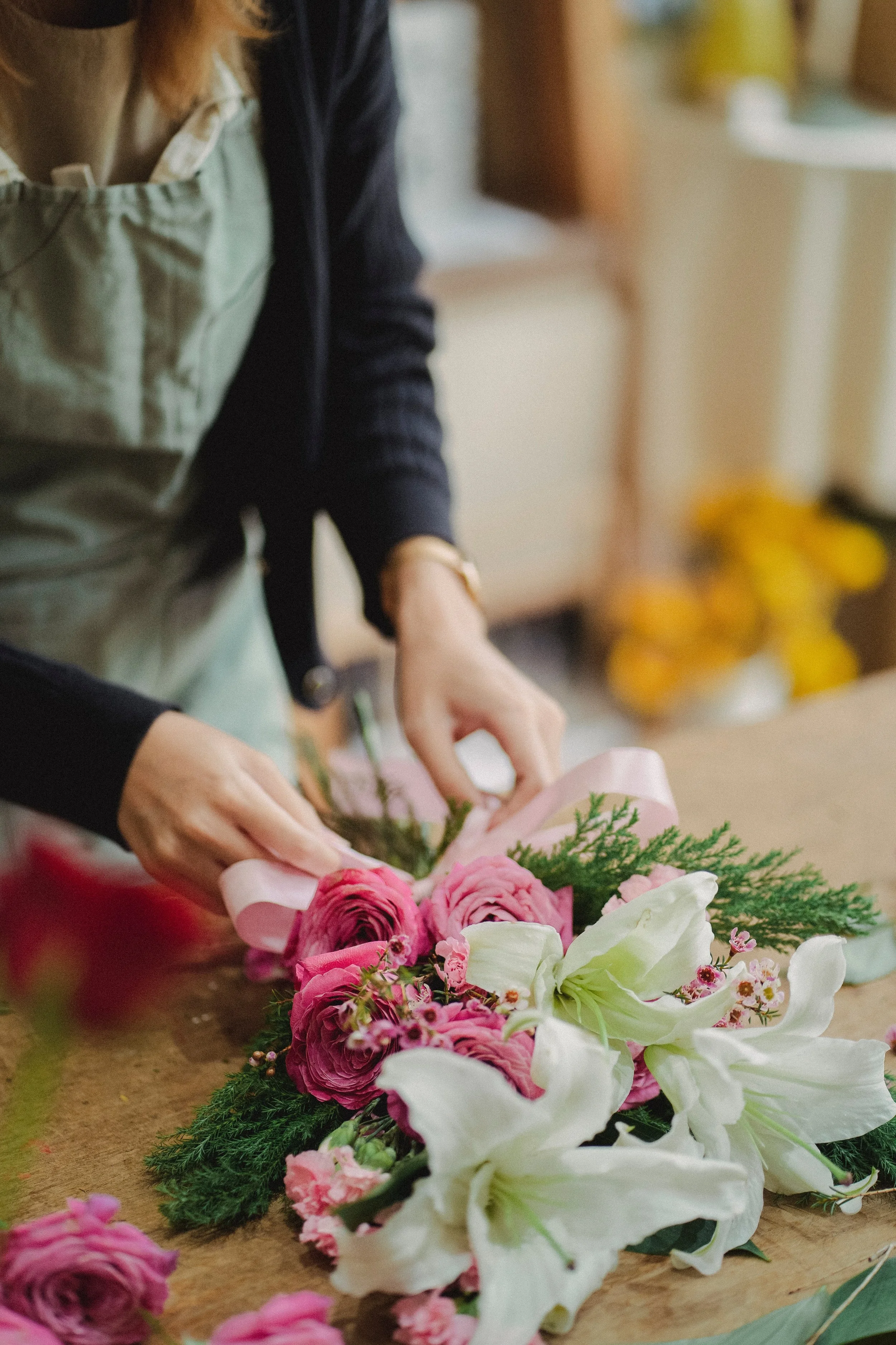 Image of a florist tying a pink bow on a bunch of pink roses and lillies