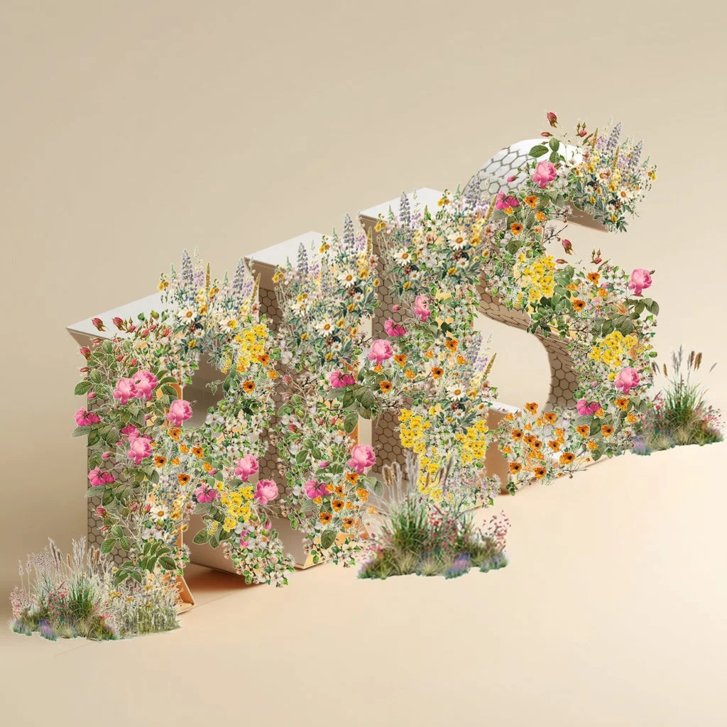 A decorative 3D letter design made of cardboard with colorful flowers and plants growing on and around it.