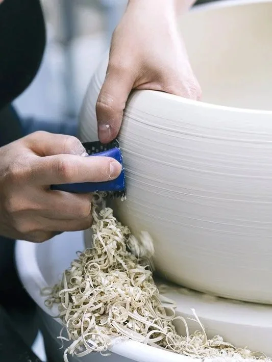 Clay Studio Leiden pottery student wheel-throwing a small conical shape in porcelain as her teacher carefully watches her