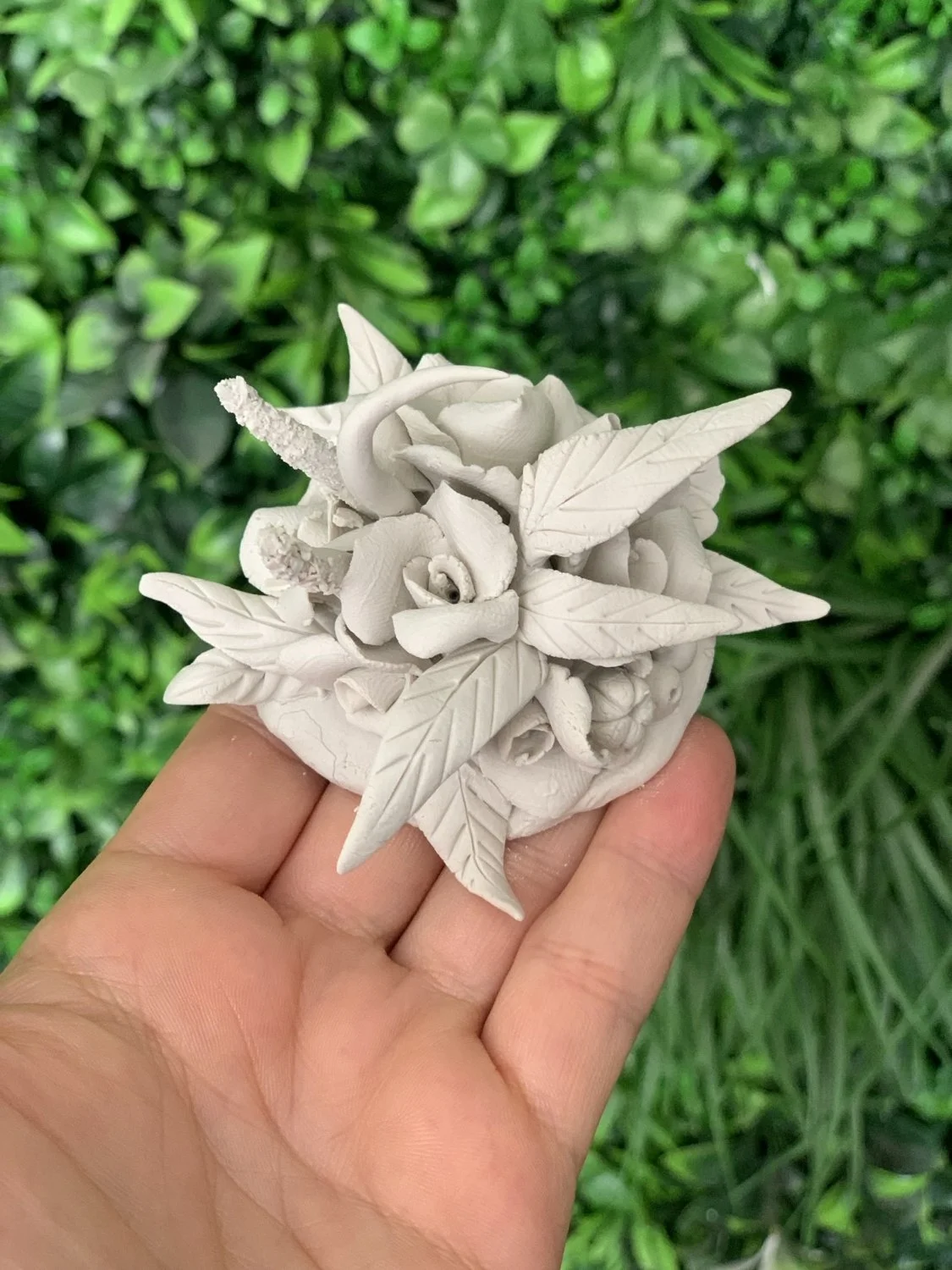 close up of a bouquet of beautiful handmade porcelain flowers against a green plant wall