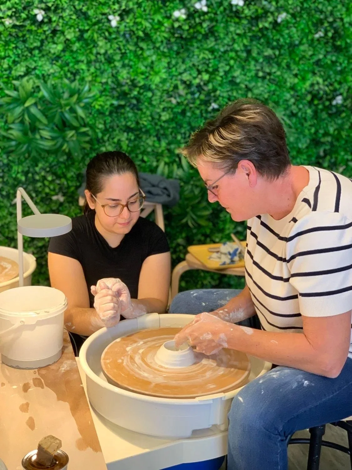 Clay Studio Leiden pottery student wheel-throwing a small conical shape in porcelain as her teacher carefully watches her
