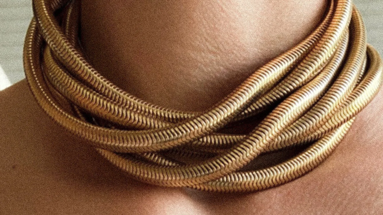 Close-up of multiple gold-colored necklaces resting around a person's neck.