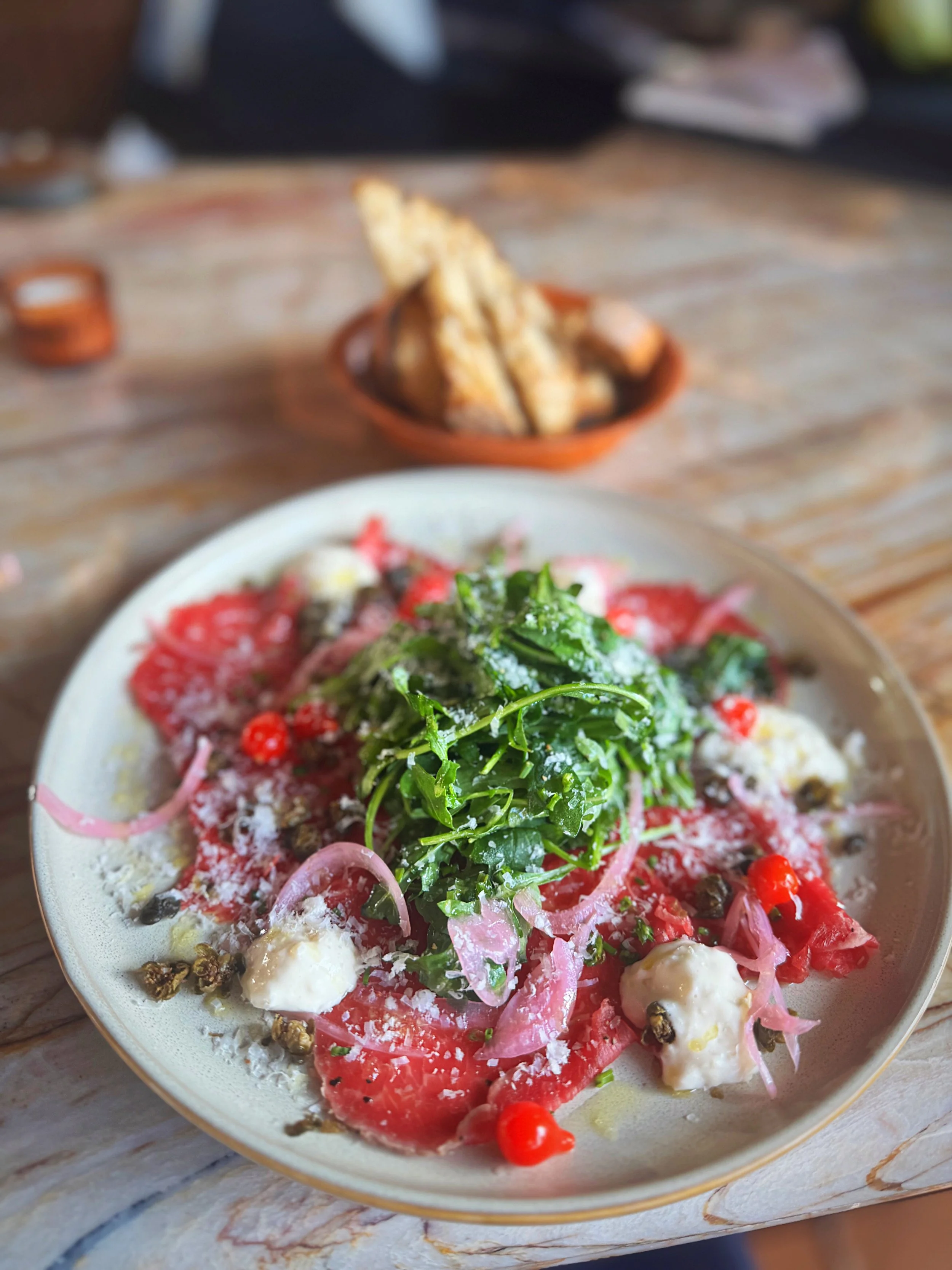 Pepper Crusted AAA Beef Carpaccio with Arugula, Fried Capers, Drop Peppers, Shallot & Garlic Crostini