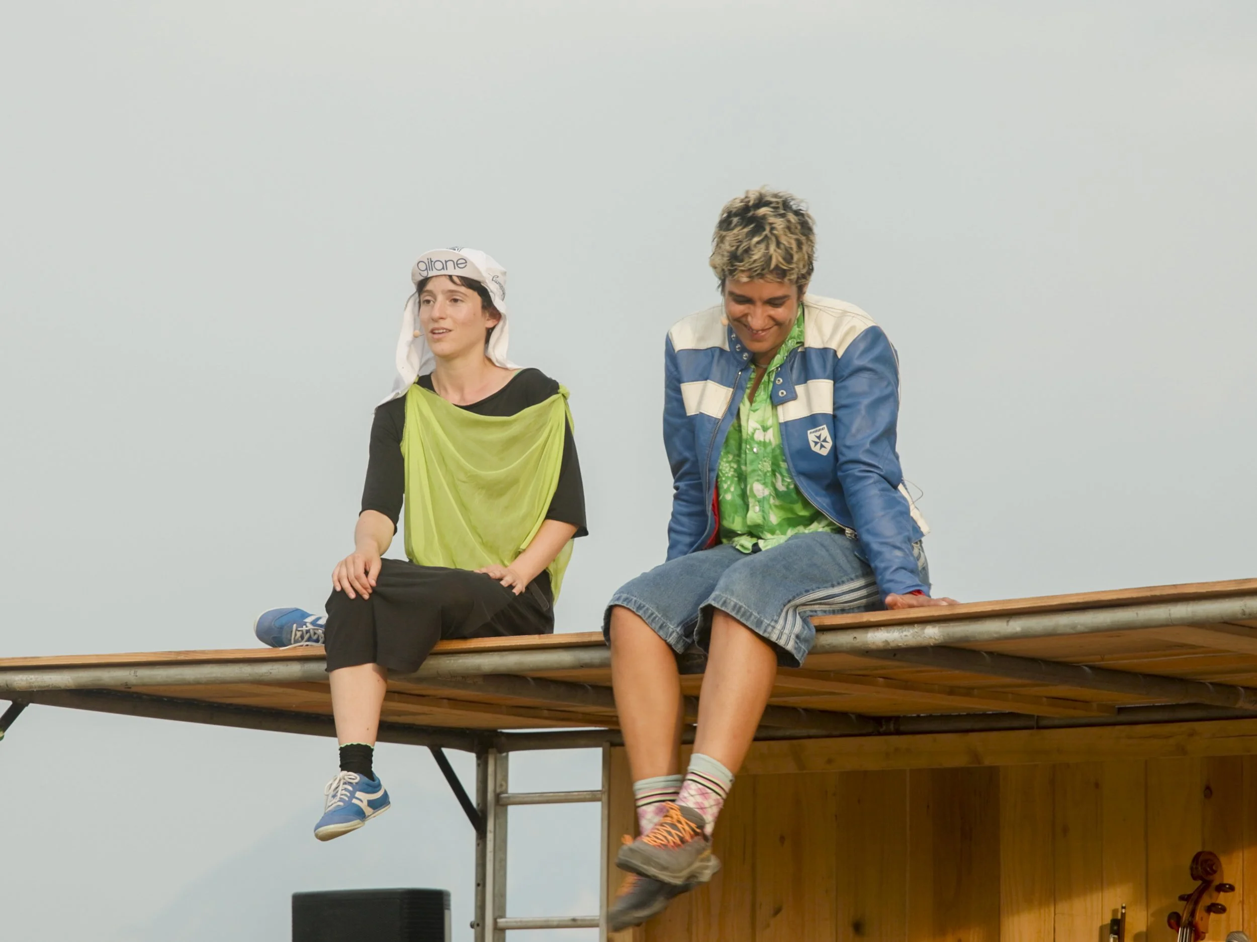 Two children sitting on a wooden platform, one girl and one boy, with a blank sky background.