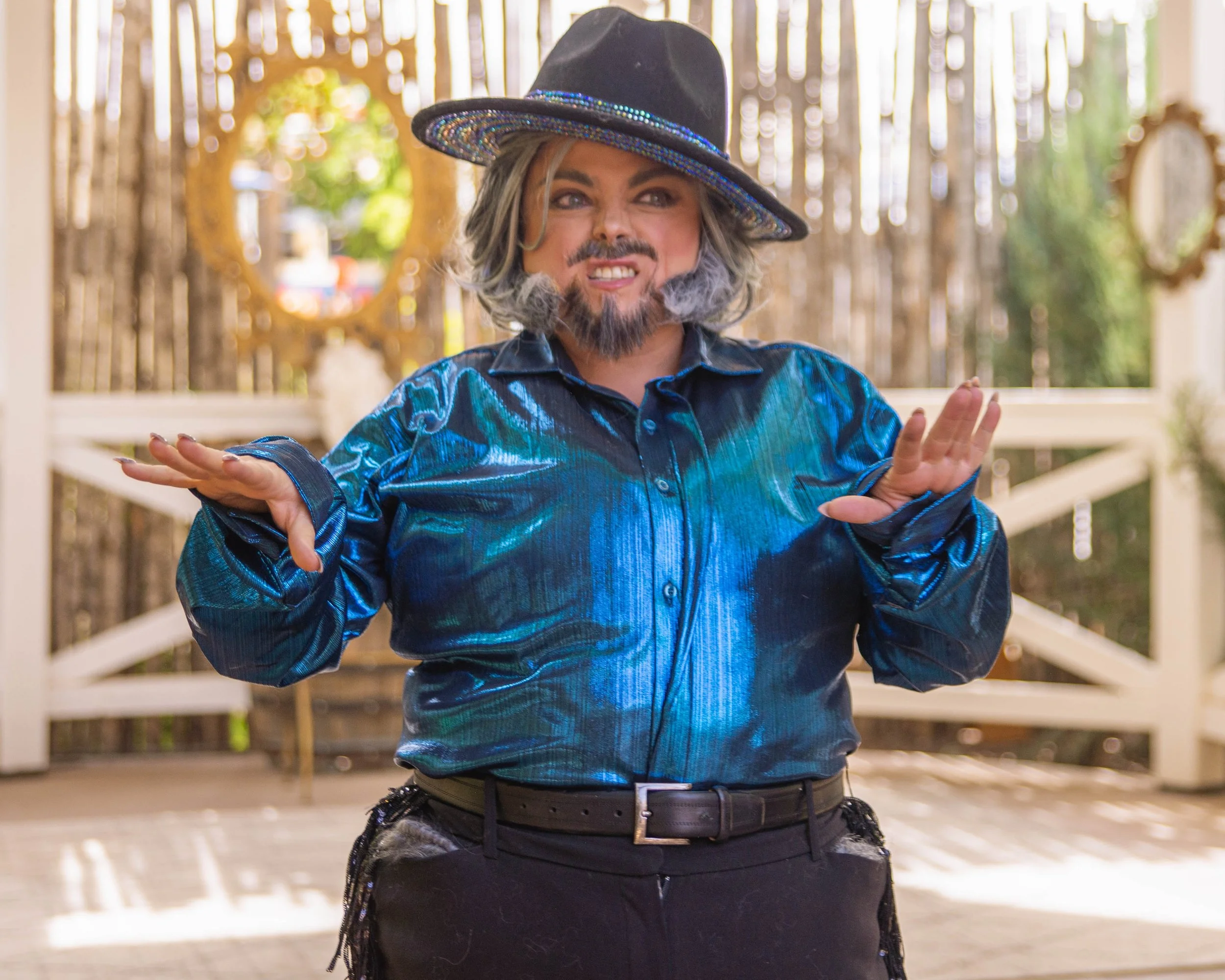 Bearded drag king growling in a performance. Wearing satin blue top, black pants, black & rhinestone hat.