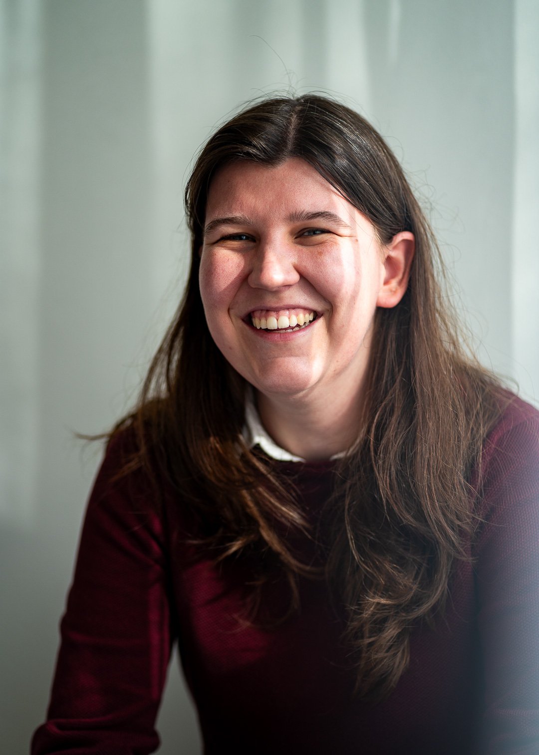 Portret van een lachende jonge vrouw met bruin haar en een blauwe achtergrond.