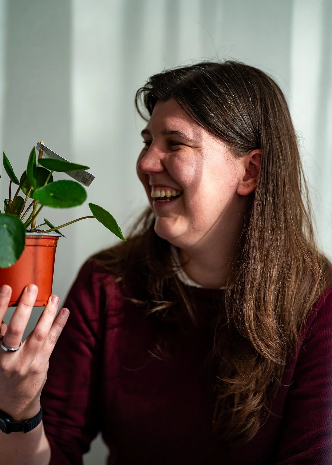 Een vrouw met bruin haar die lacht en naar een groene plant in een oranje pot kijkt.