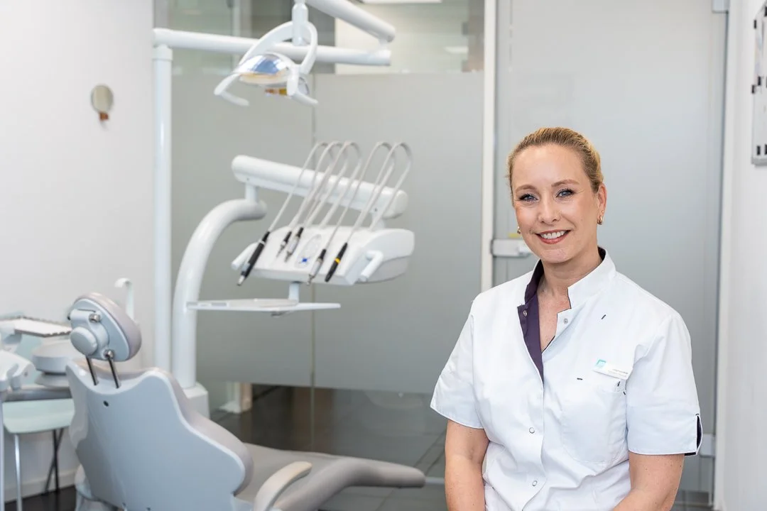Een vrouwelijke tandarts poseert in een tandartspraktijk met tandheelkundige apparatuur op de achtergrond. - bedrijfsfotografie