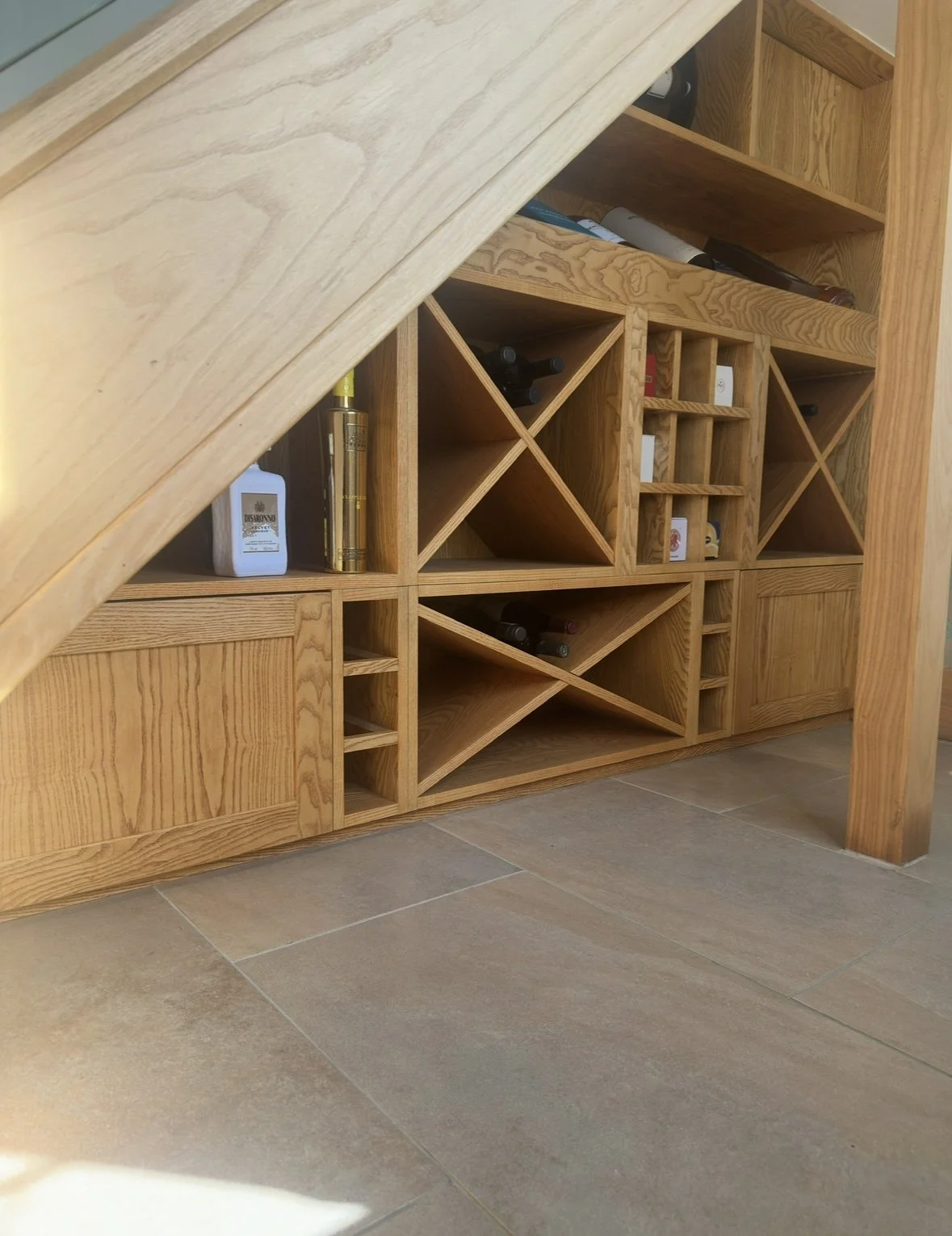 Ash veneer bespoke under stairs wine display complete with led strip lighting, push to open cabinets, open wine storage and five piece shaker detail