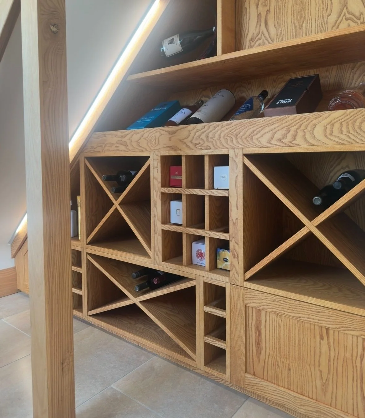Ash veneer bespoke under stairs wine display complete with led strip lighting, push to open cabinets, open wine storage and five piece shaker detail