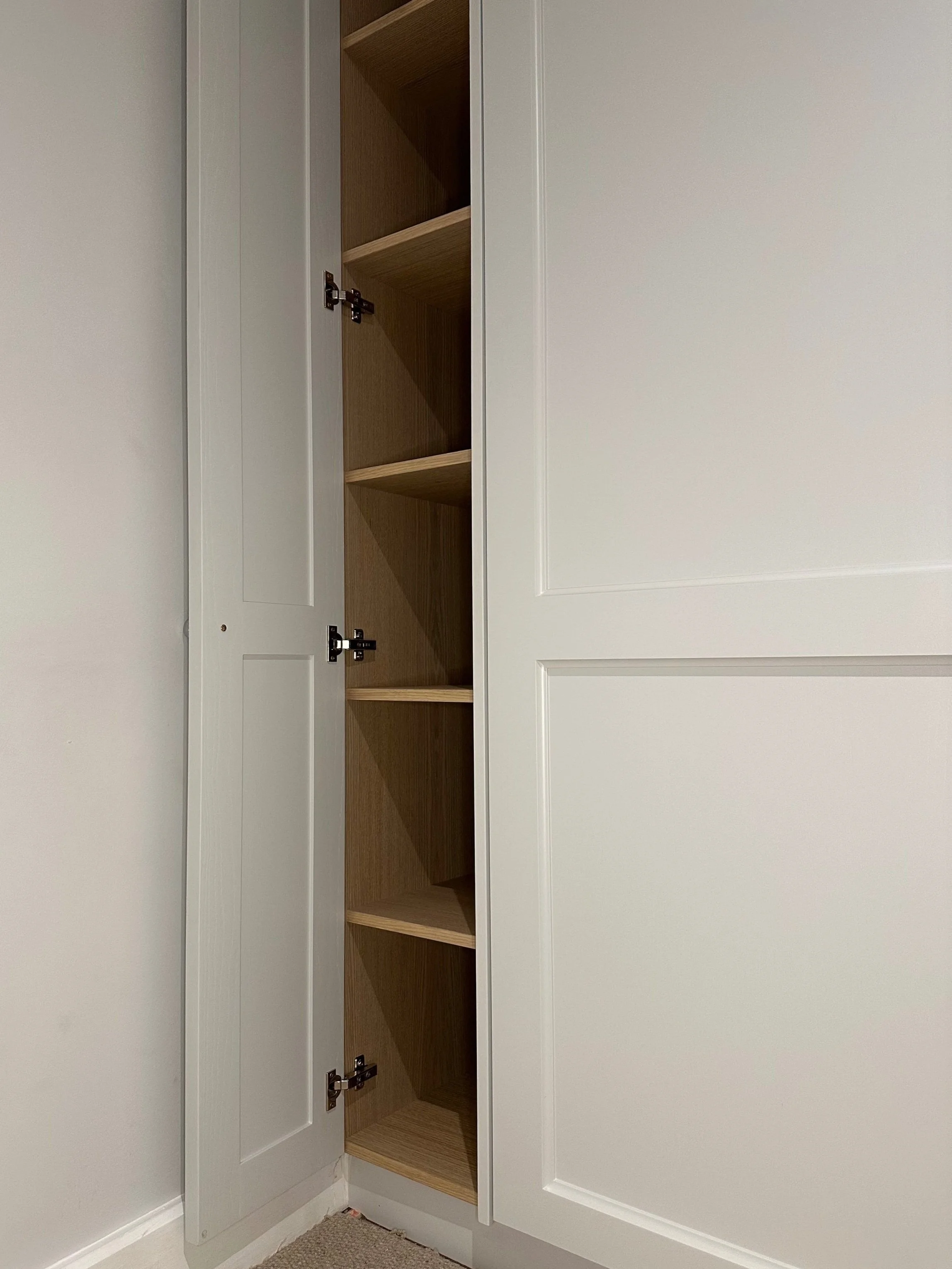 Open white cabinet with four wooden shelves inside, in a room with beige carpet and a white wall.