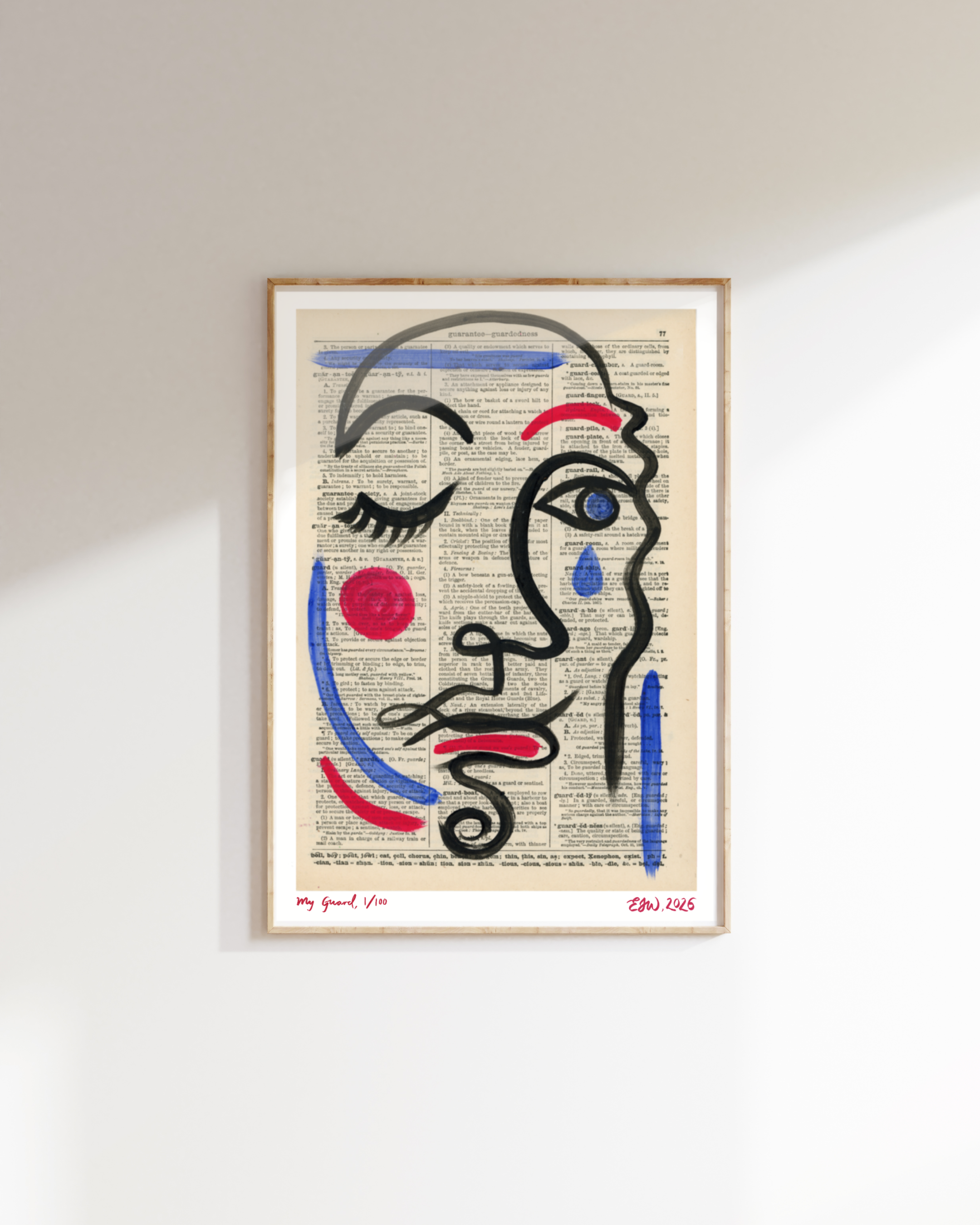 Framed artwork by Emma Winterschladen on a white wall depicts a woman's face outlined in black paint, with red cheeks, blue tears, and a black curl as hair, displayed over a page of dictionary text.