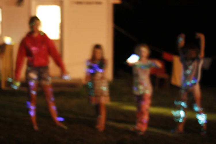 campers wrapped in glow sticks, dancing in the camp dark