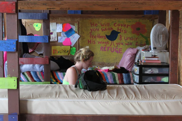 andie in her old pagweak bunk, a wall of camper notes behind her