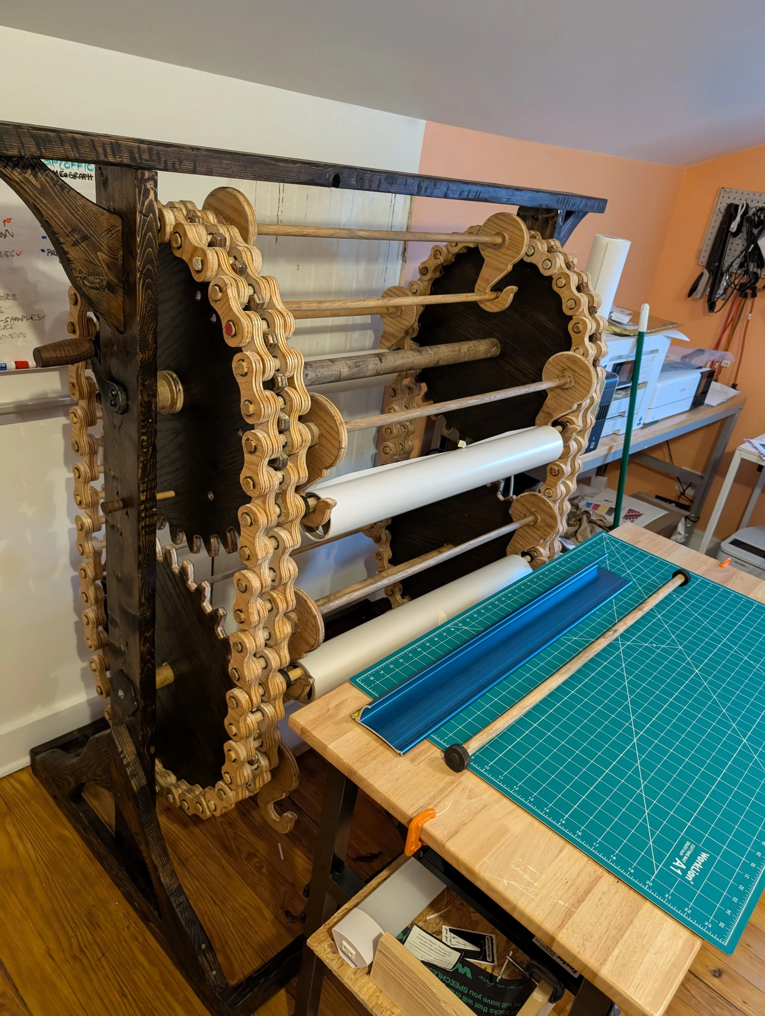 A crazy contraption we made to carousel laminate rolls! Made for a friend and a super fun build.  Wooden chain on plywood gears. Plywood hooks milled on the cnc. 