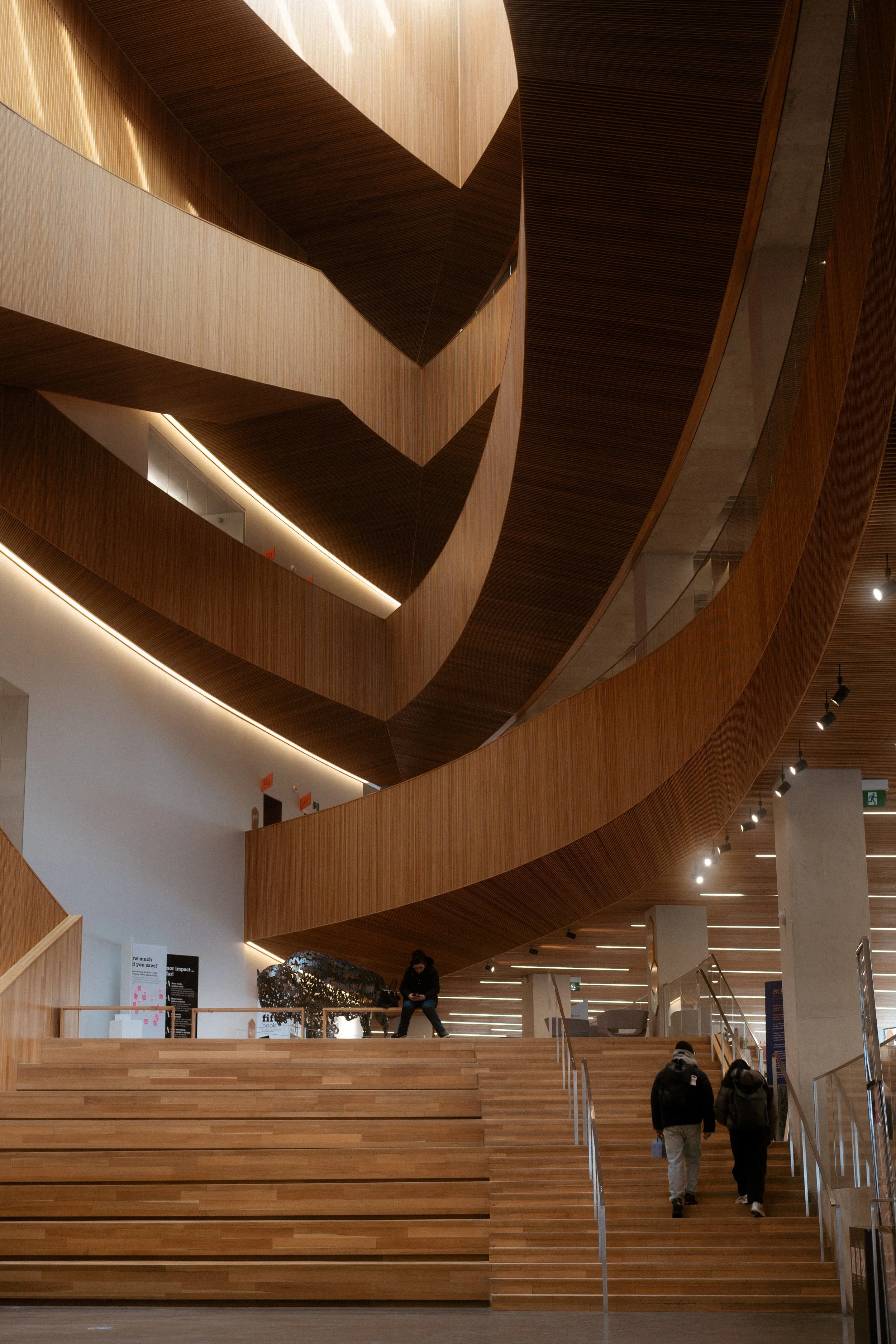 Calgary Central Library architecture interior with curved wood staircases and flowing geometry, capturing how material, light, and circulation shape movement through the space.