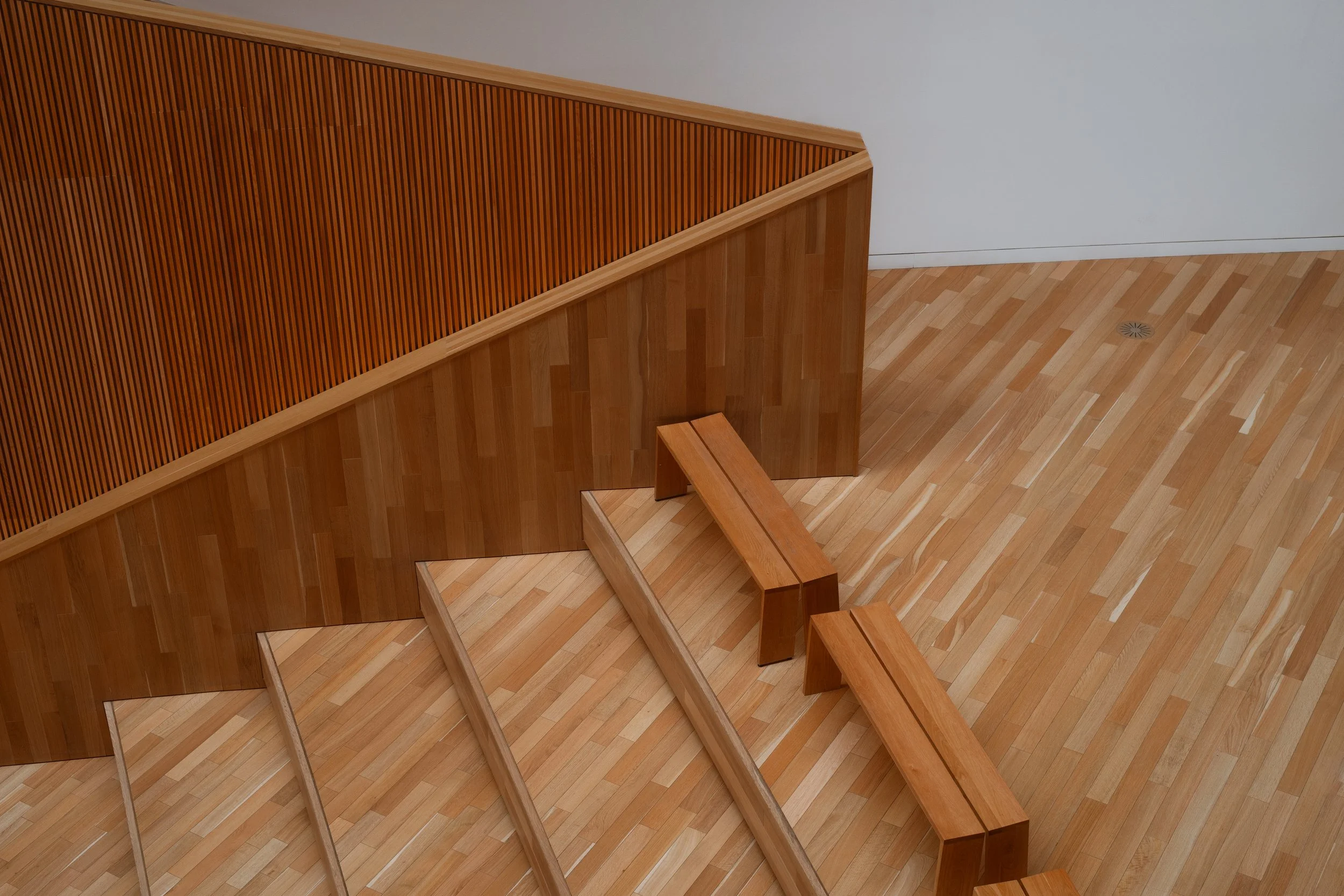 Calgary Central Library interior showing stepped wood entrance leading into the central staircase, with integrated seating and vertical slat detailing.