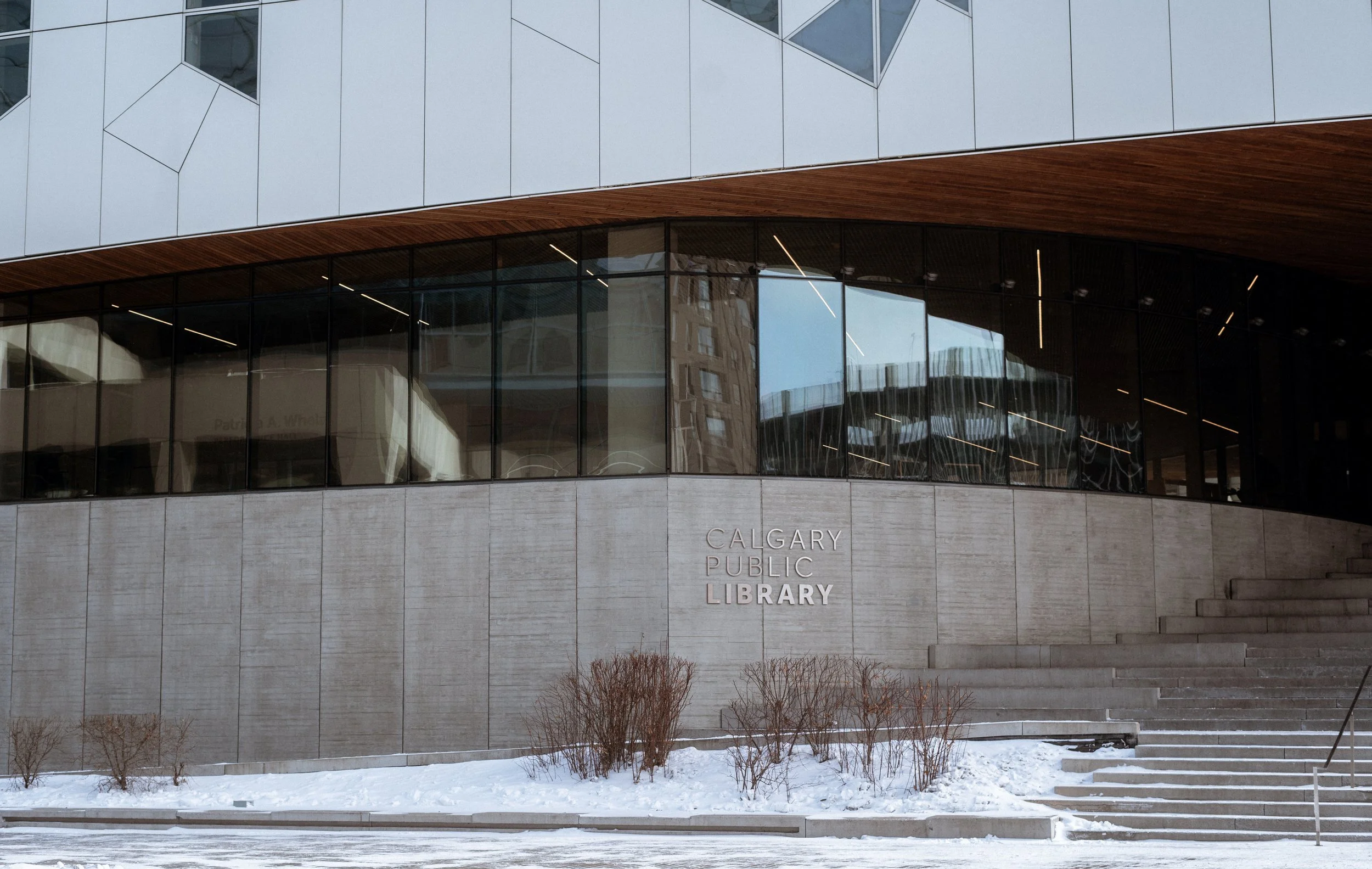 Exterior of Calgary Central Library in downtown Calgary, featuring curved glass façade, concrete base, and wood soffit defining the building’s architectural identity.