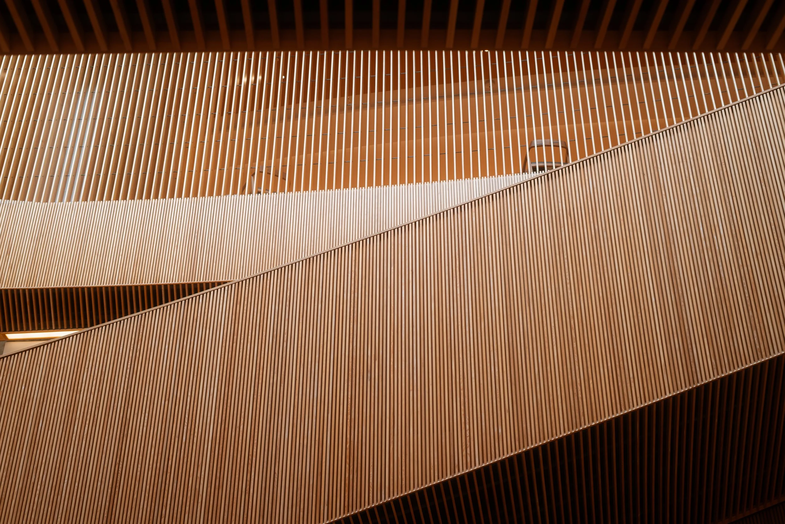 Calgary Central Library interior detail of vertical wood slat architecture along the staircase, with the Great Reading Room visible above.