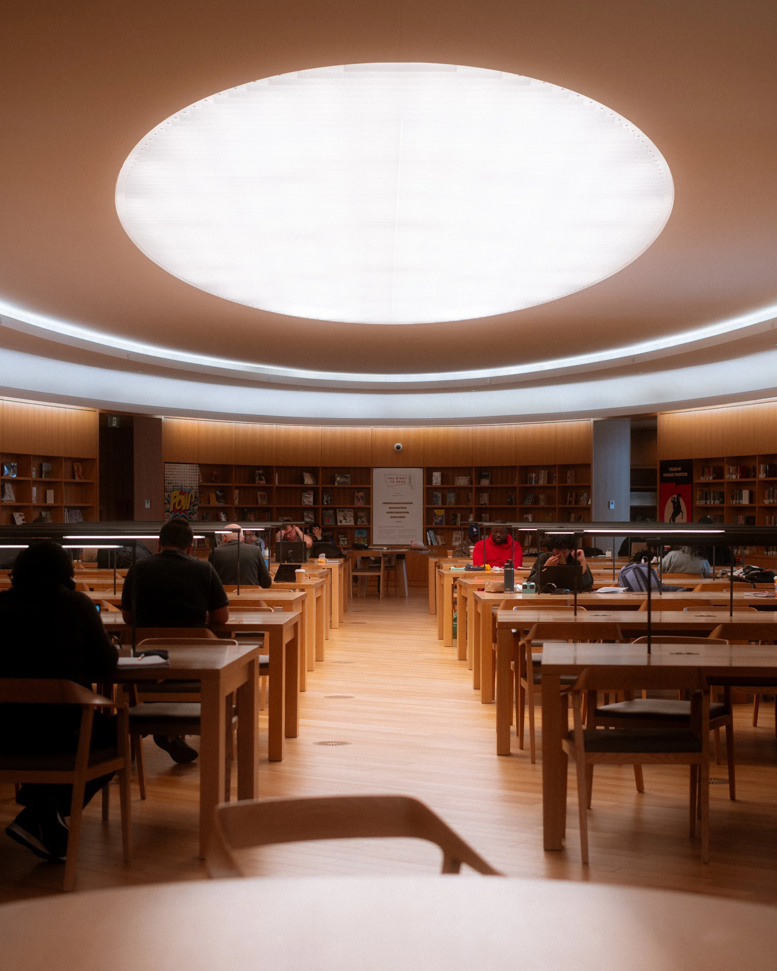 Calgary Central Library Great Reading Room interior with circular oculus skylight, even diffused light, and study tables arranged beneath the curved wood ceiling.