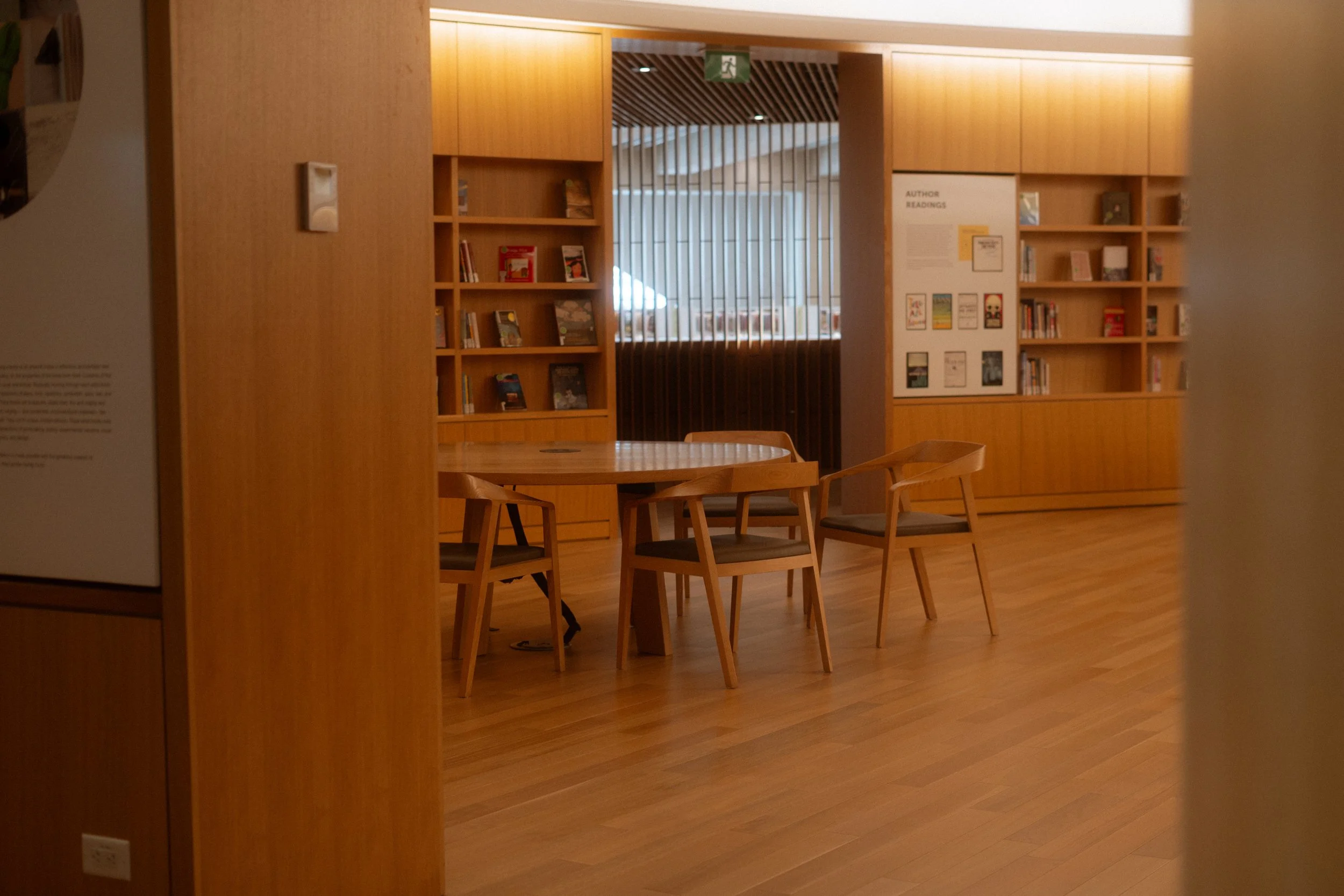 Interior of Calgary Central Library Great Reading Room showing wood-lined walls, integrated shelving, and quiet study area with table and seating.