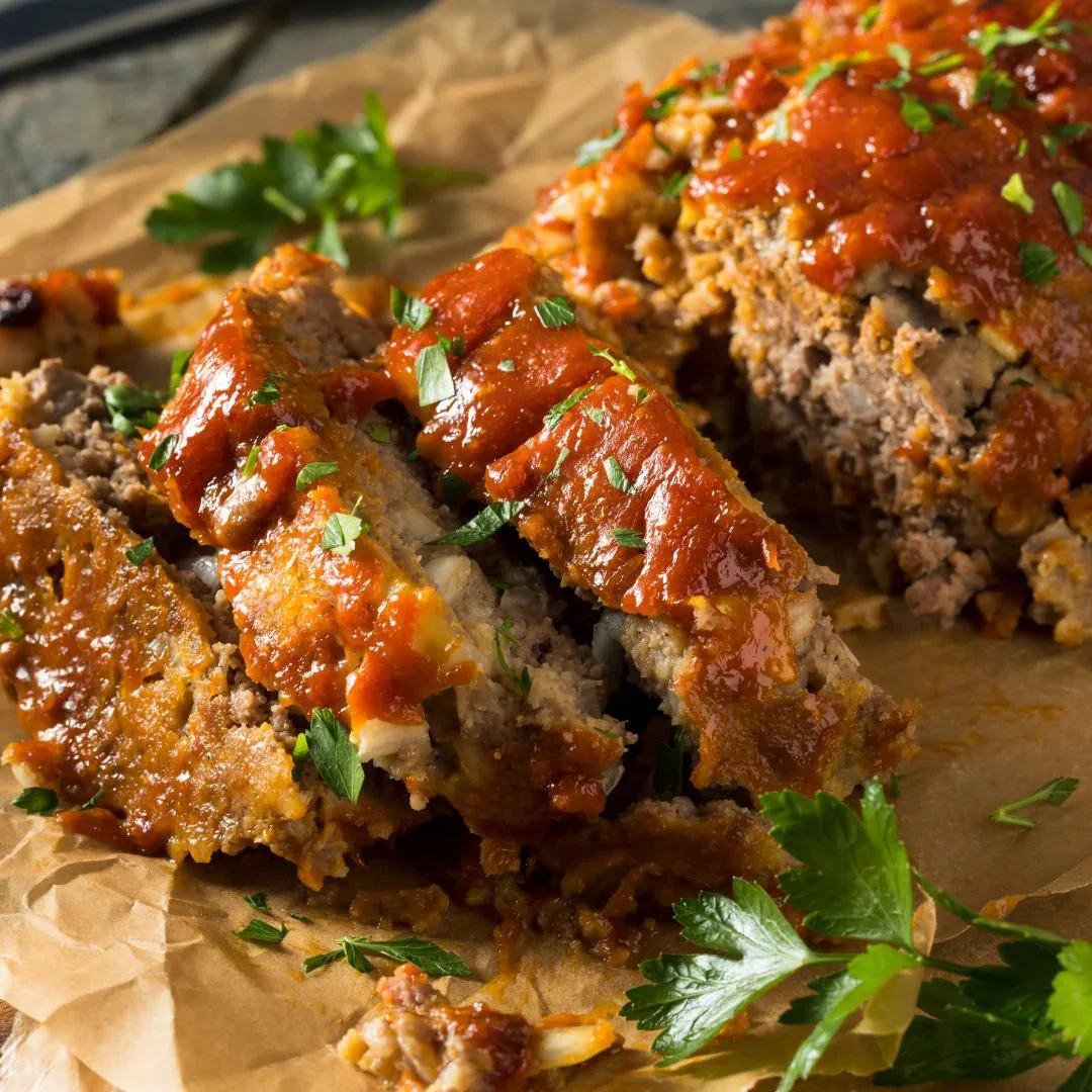 A meatloaf loaf topped with tomato sauce, garnished with parsley, with a slice cut out showing the inside.