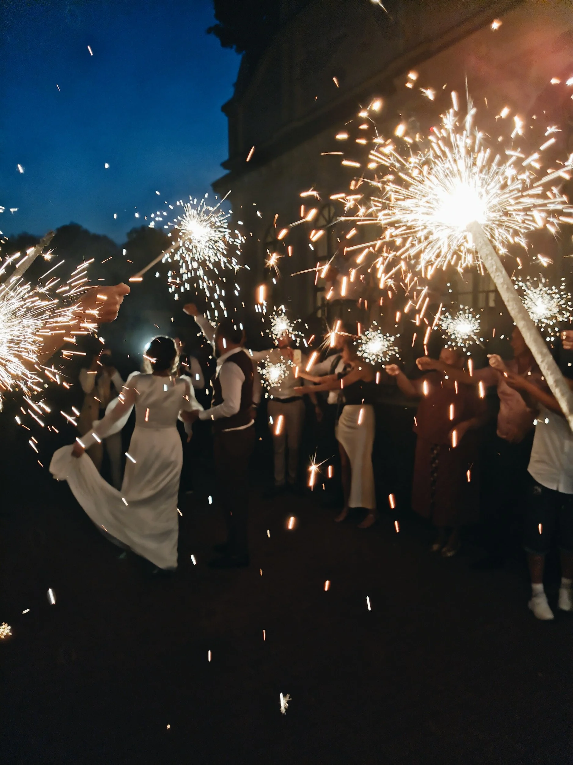 People celebrating with sparklers and fireworks during an evening outdoor event, possibly a wedding or festive gathering.