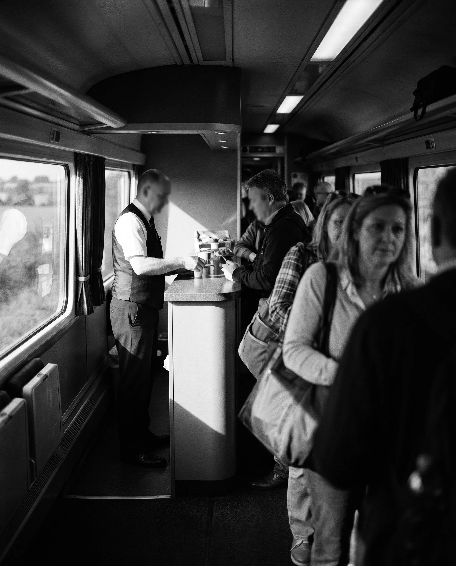Passengers queueing at a train buffet counter served by one crew member