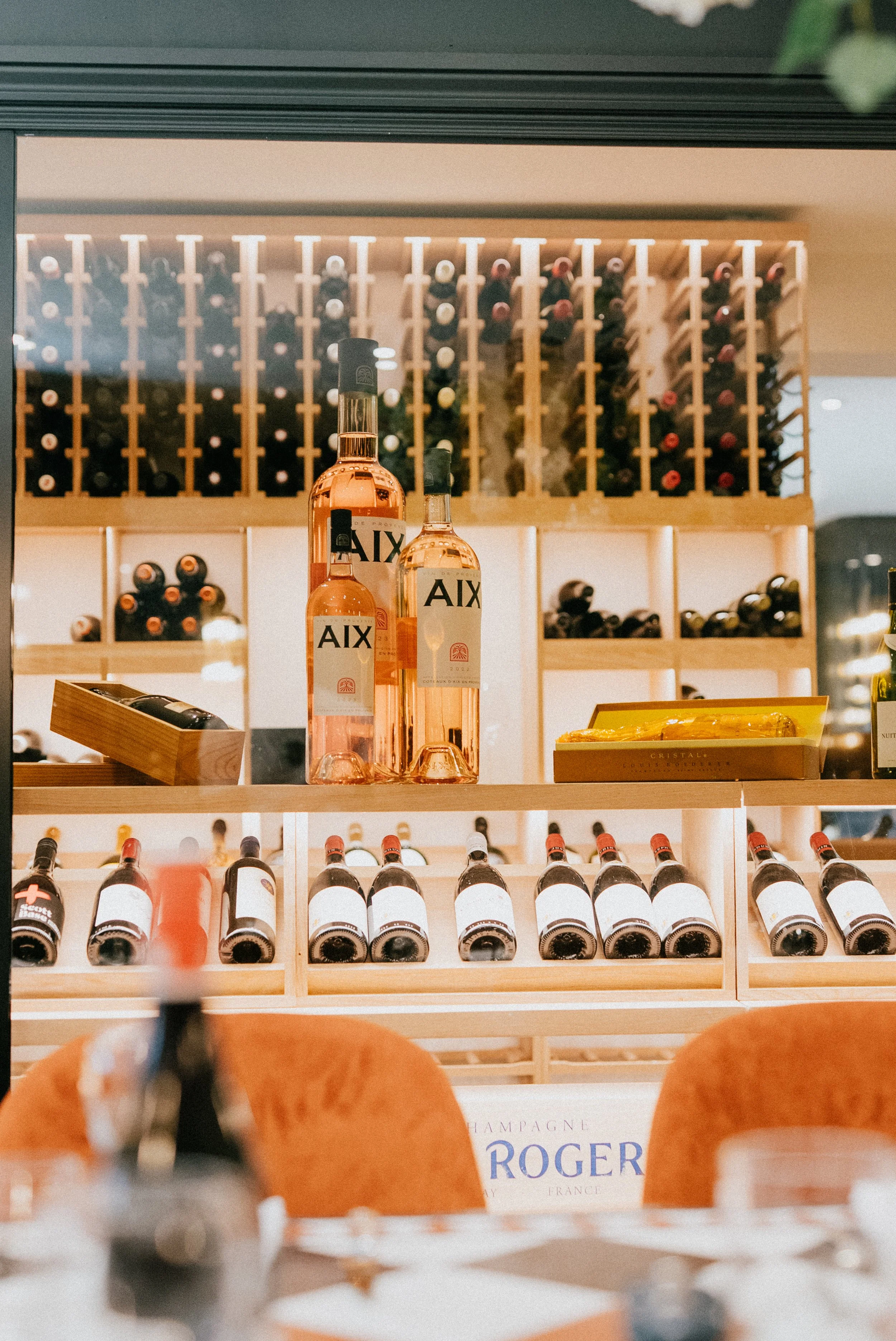Wine bottles on a wooden shelf in the RT Cafe grill Cellar with a wine rack in the background at a wine store or restaurant.