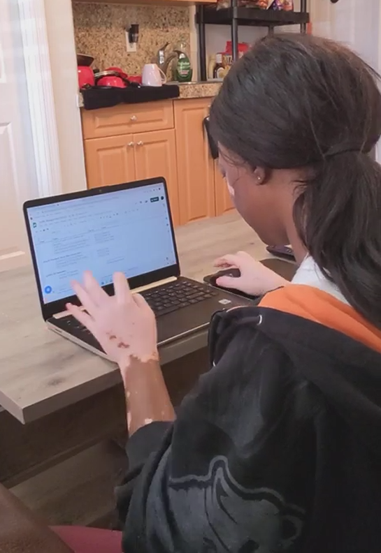 a woman sitting at a computer at her kitchen table typing