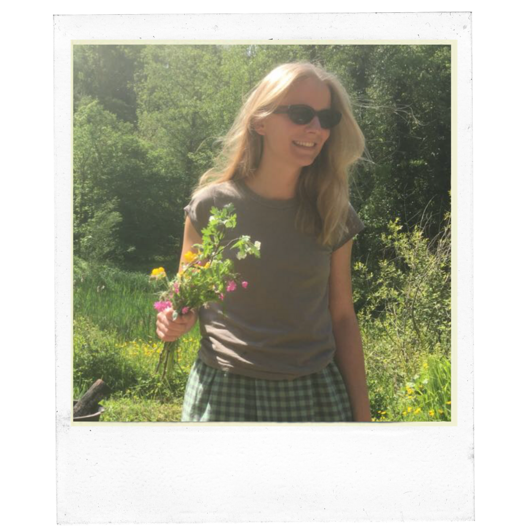 Smiling person wearing sunglasses holding flowers in a sunny garden.
