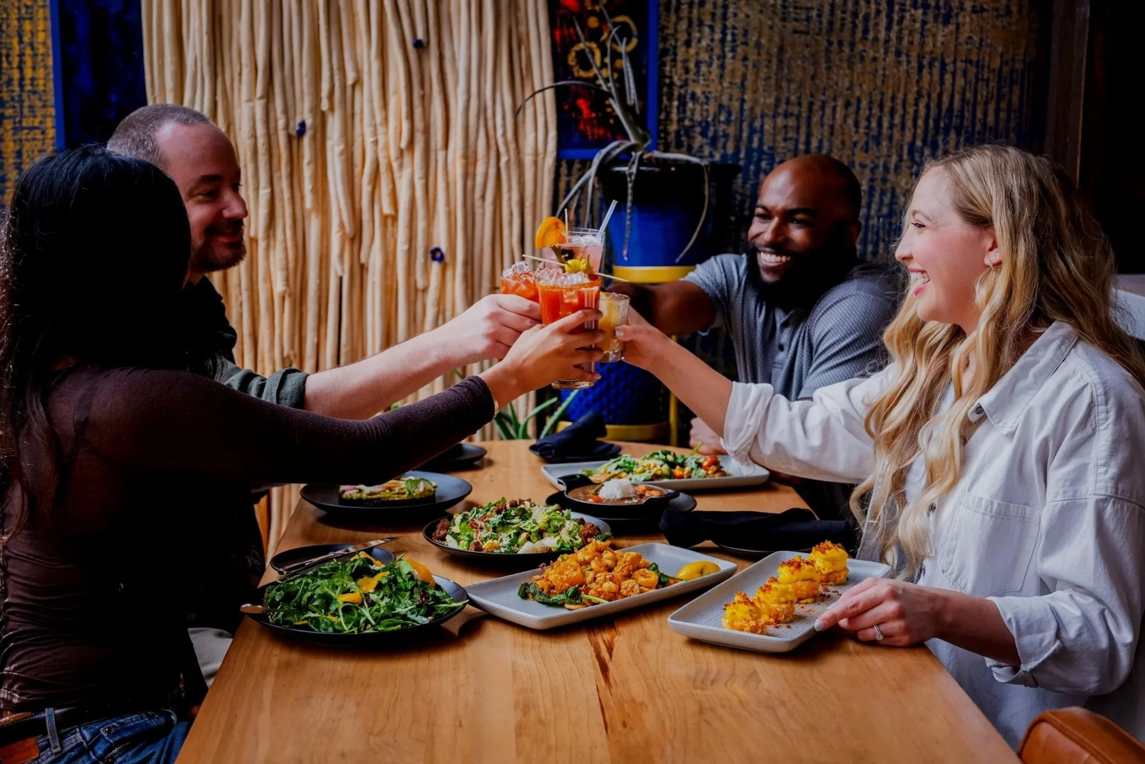4 people eating at Milk & Honey with several appetizers and cheersing with drinks