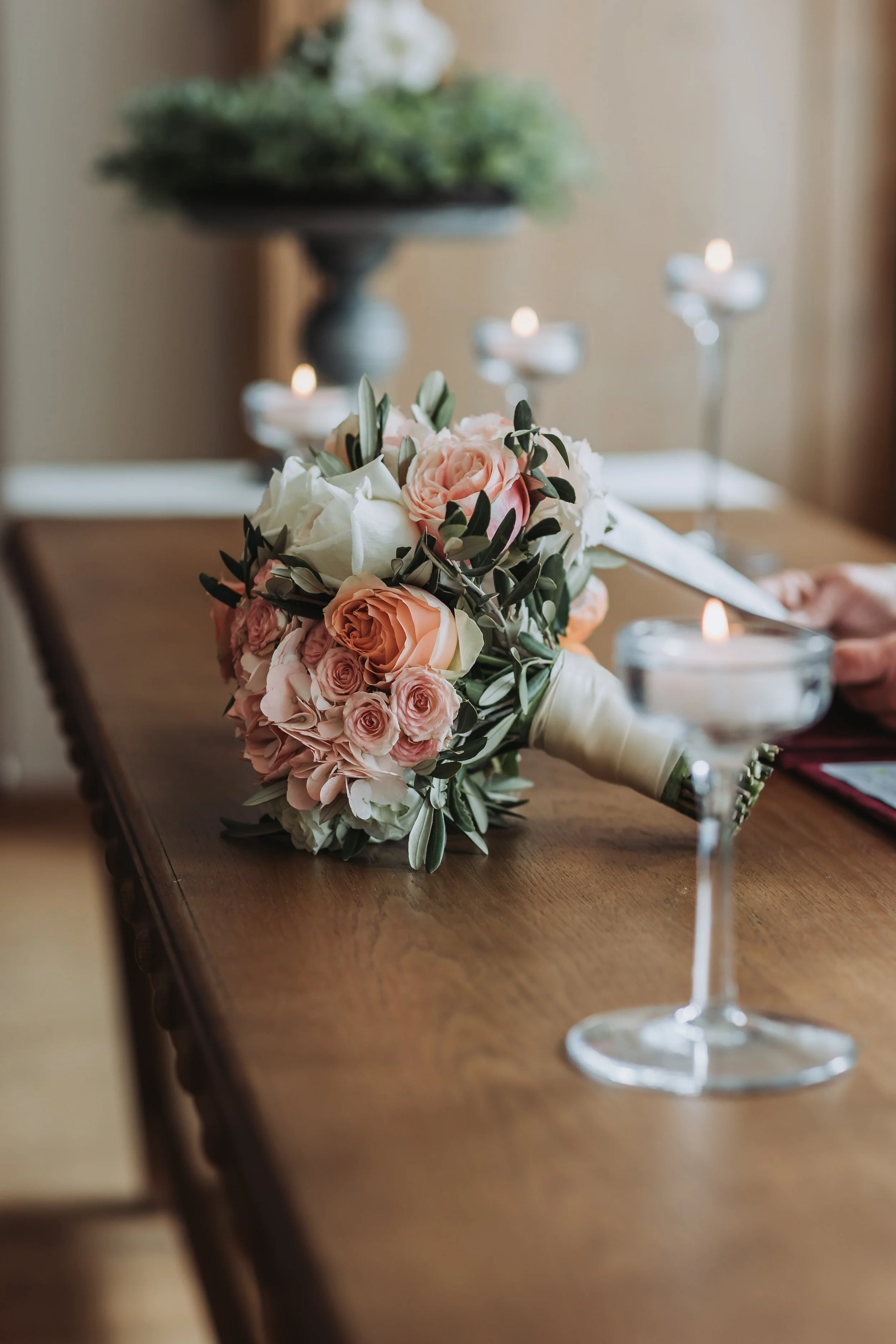Ein Blumenstrauß mit weißen und pinken Blumen auf einem Holztisch, im Hintergrund Kerzen und eine Vase.