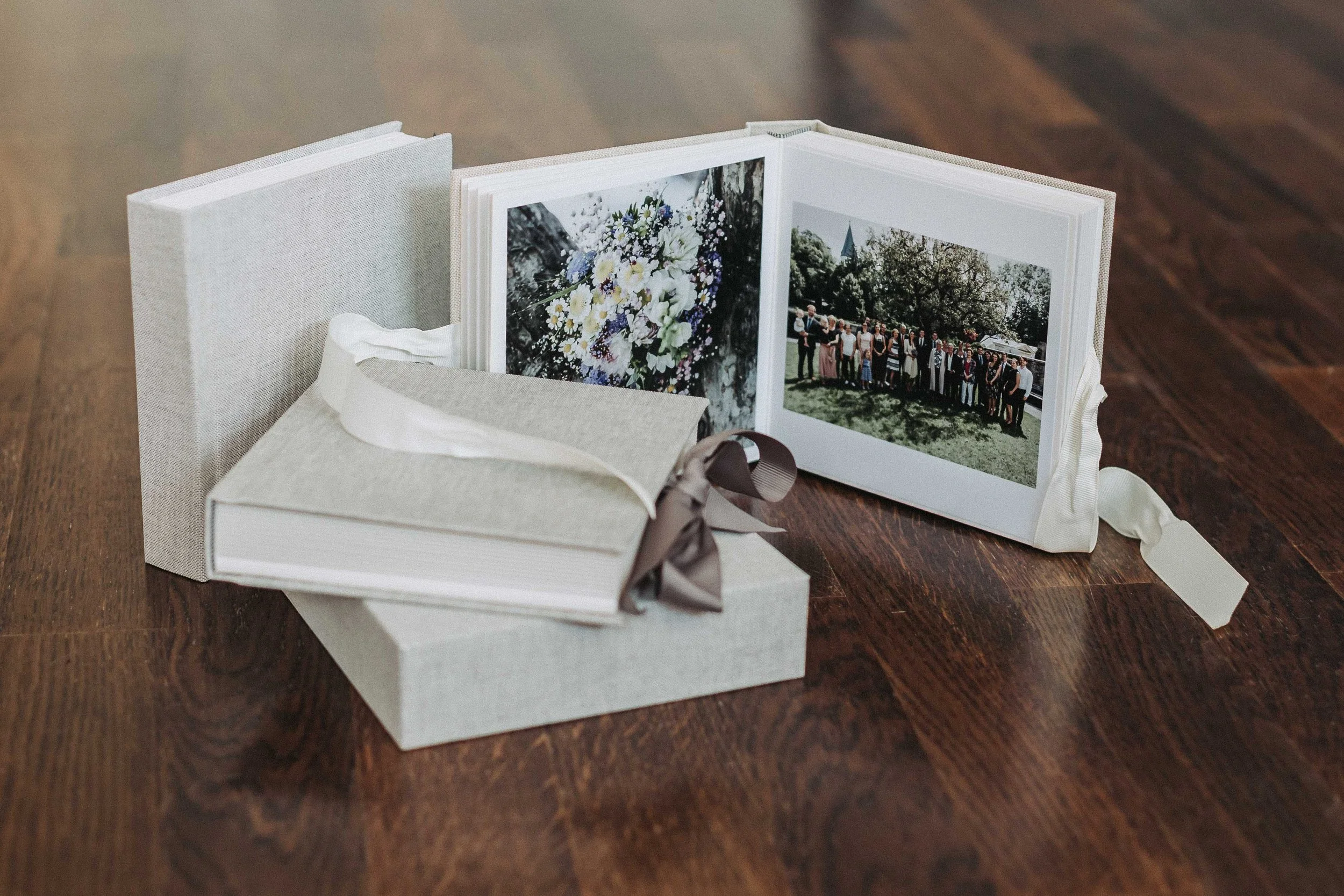 Eine offene Fotoalben auf einem Holztisch mit zwei Fotos, eines mit Blumen und eines mit einer Menschengruppe bei einer Veranstaltung.