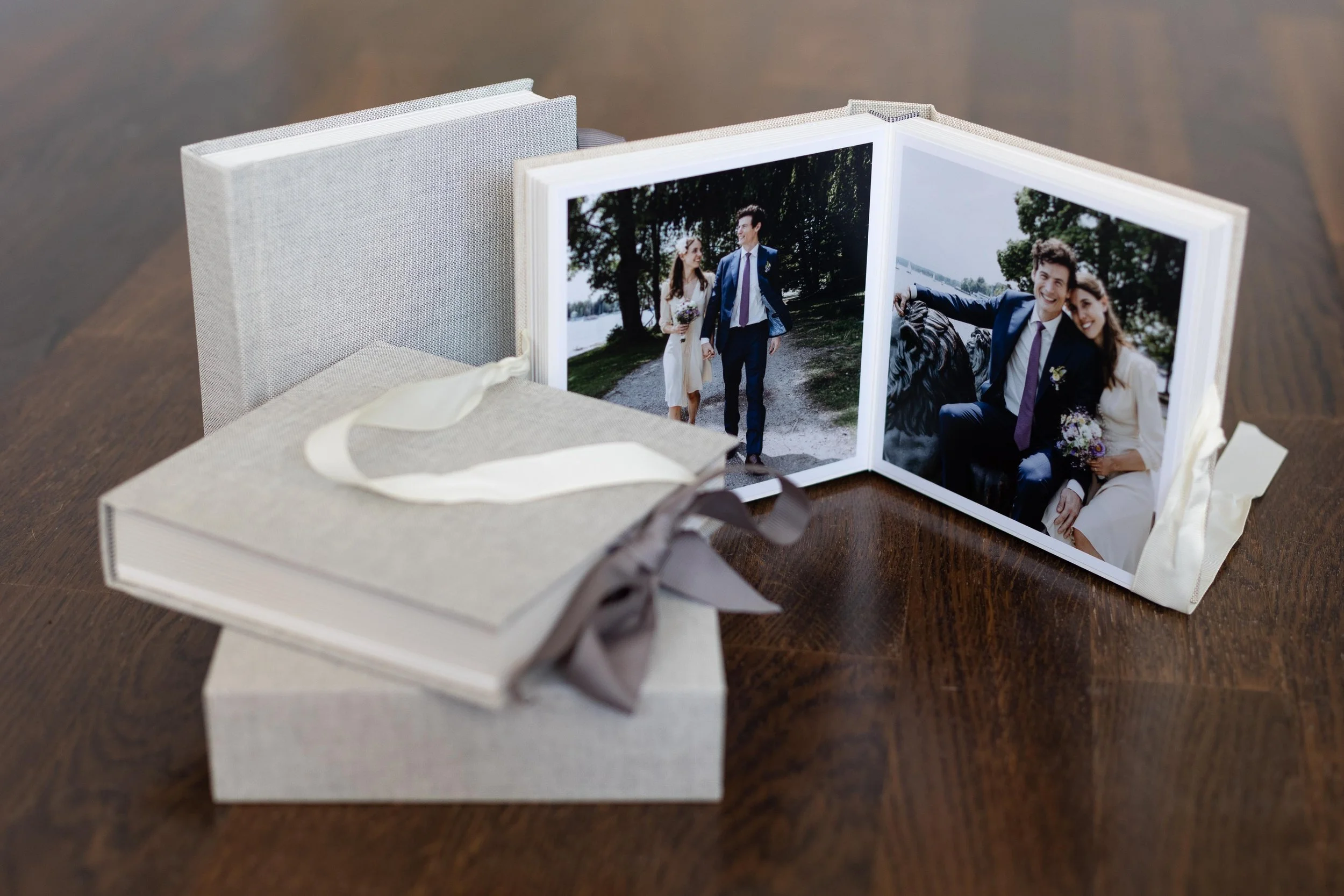 Ein aufklappbares Fotoalbum mit Hochzeitsfotos, das auf einem Holztisch liegt, neben einer Geschenkbox mit Schleife.