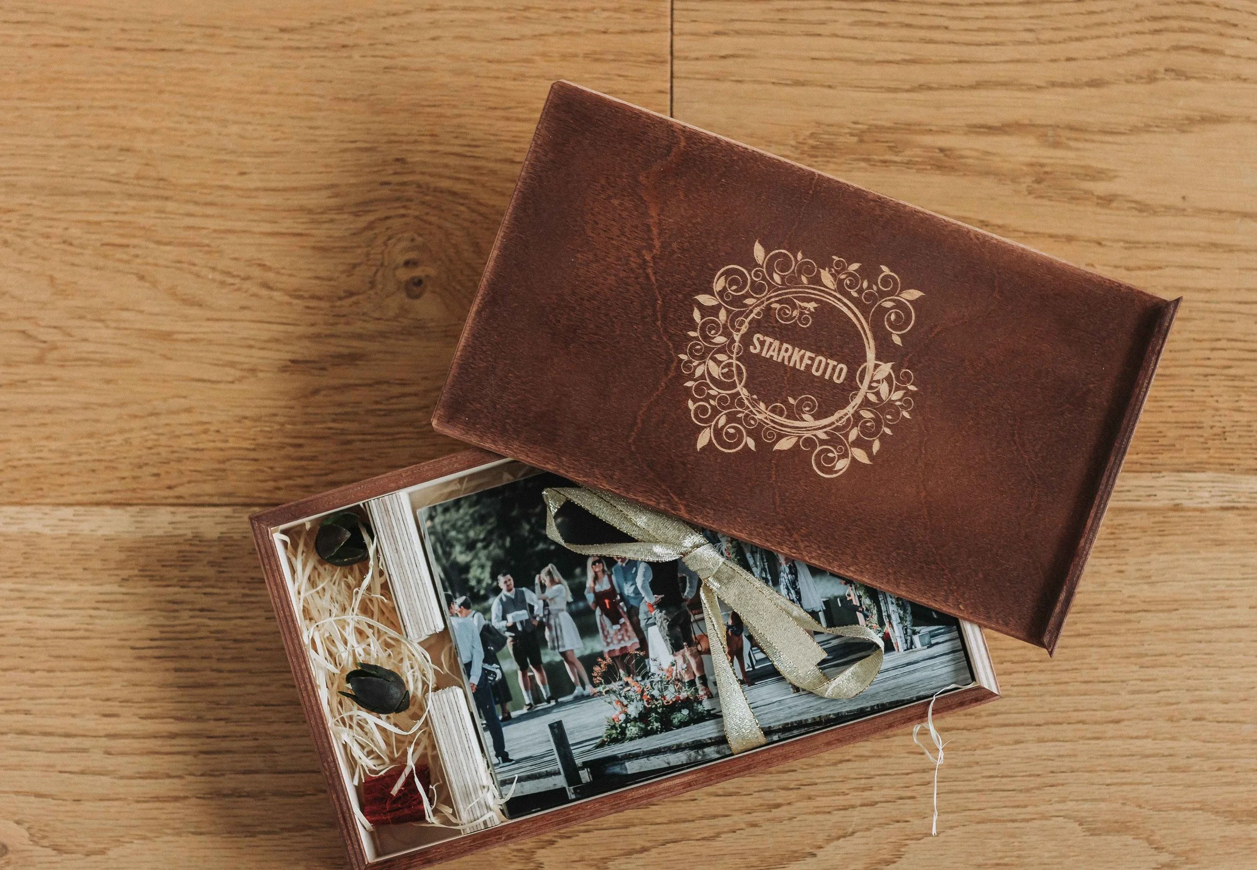 Ein Geschenkset mit Fotokarten in einer Holzschachtel, verziert mit einem goldenen Band, auf einem Holztisch. Der Deckel der Schachtel ist braun mit weißen dekorativen Elementen und der Text 'STARKFOTO'.