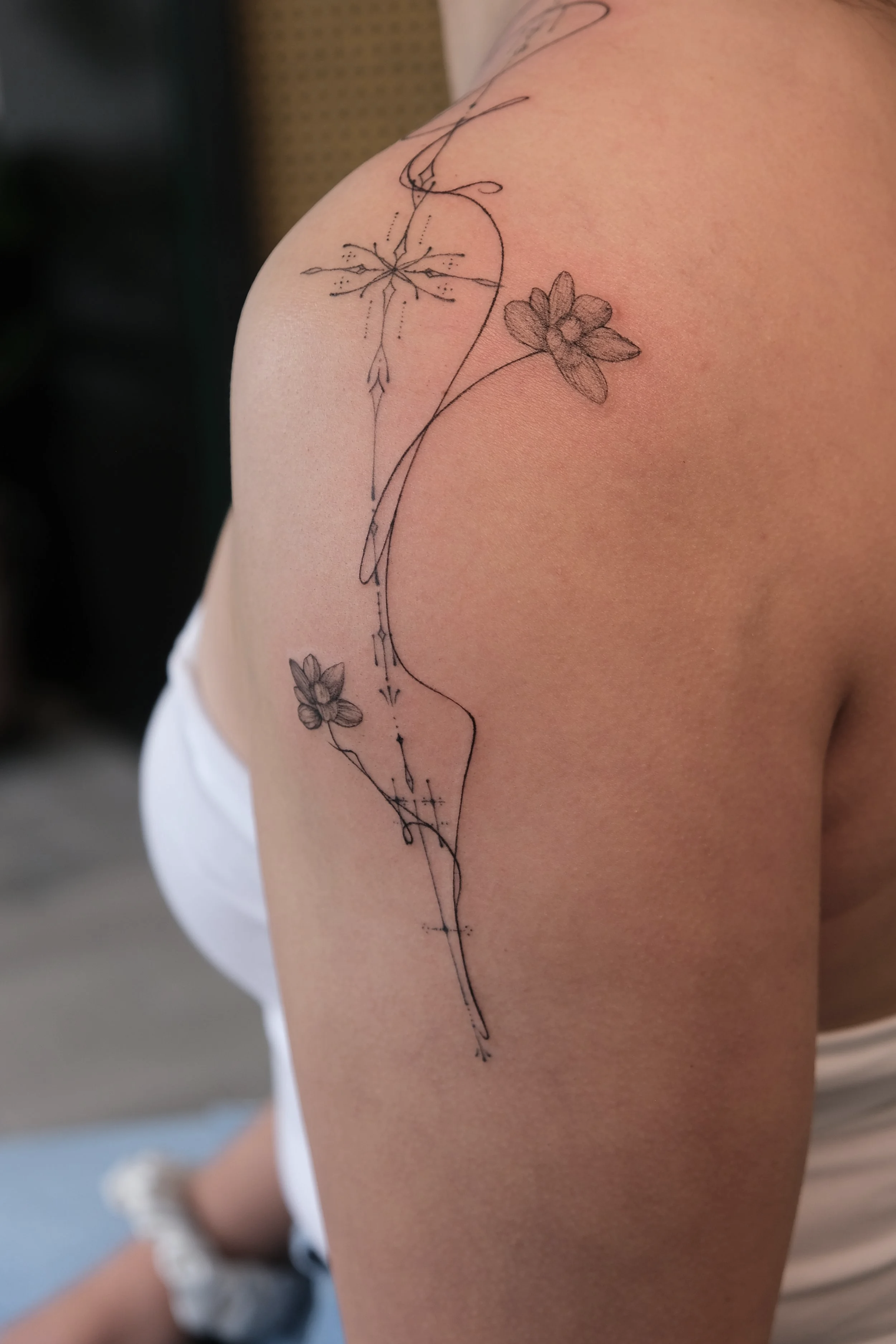 Minimalist floral tattoo on shoulder with star and line art design. single needle fine line inkpress mags studio ornamental font script smoke floral