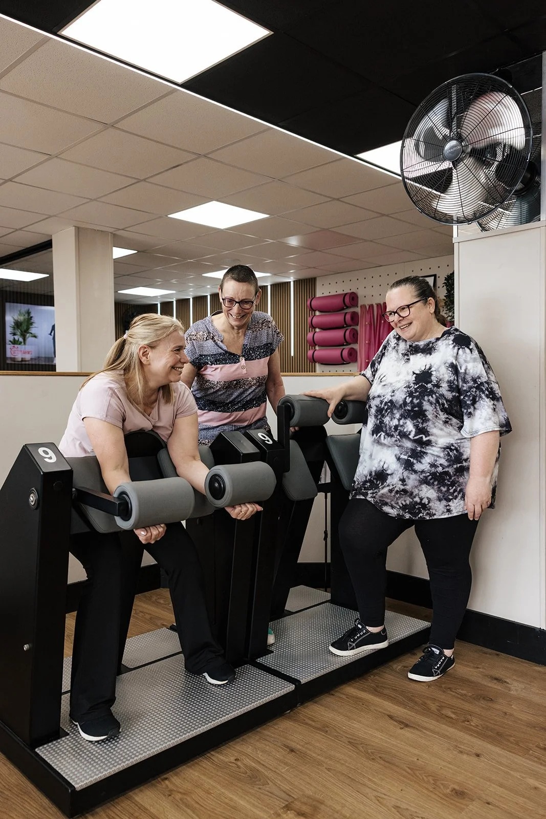 A female gym-goer smiling as she uses equipment in a bright, welcoming fitness space.