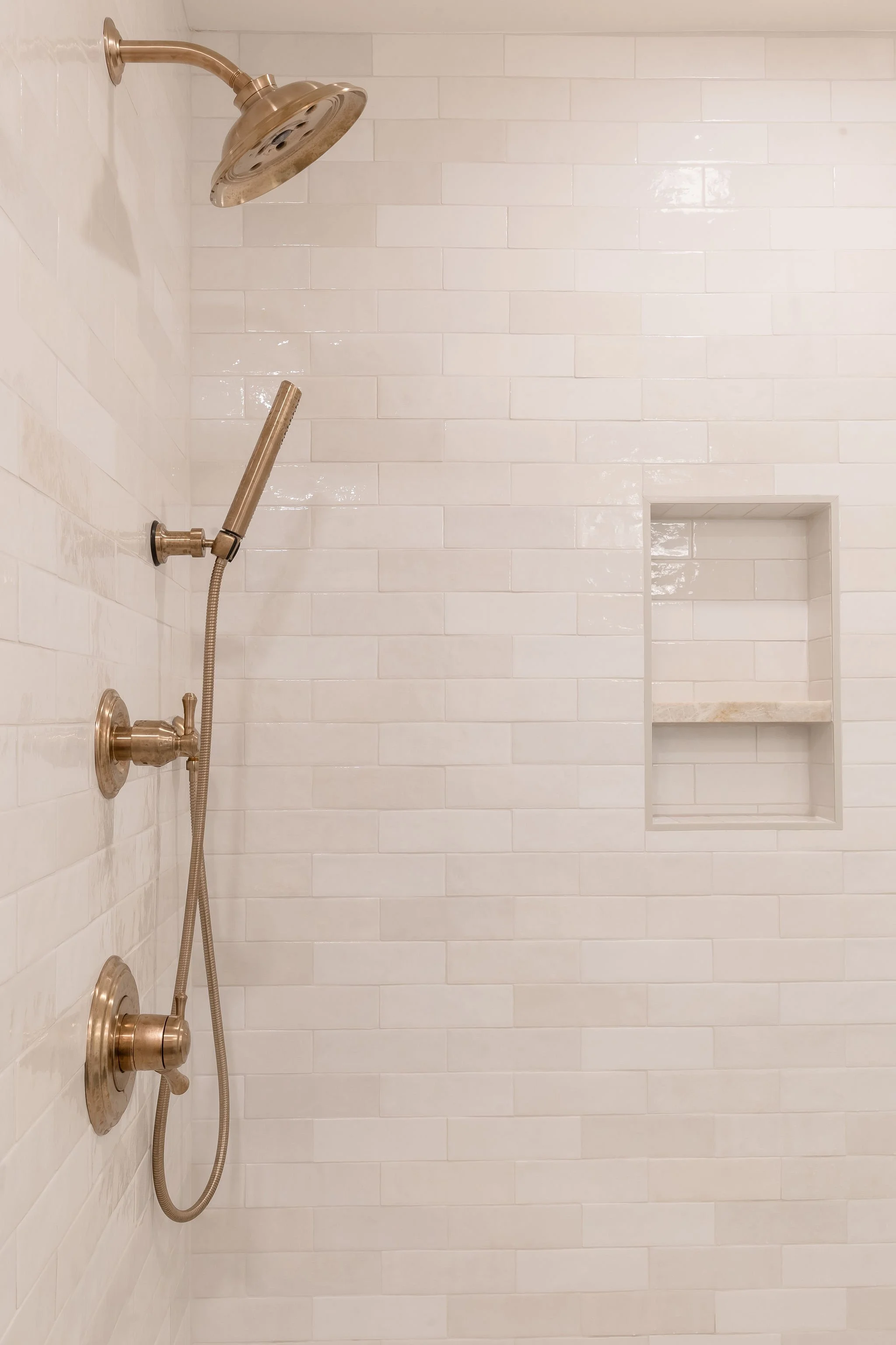 Shower with white subway tile walls, a chrome showerhead, a handheld shower wand, and built-in niche for toiletries.