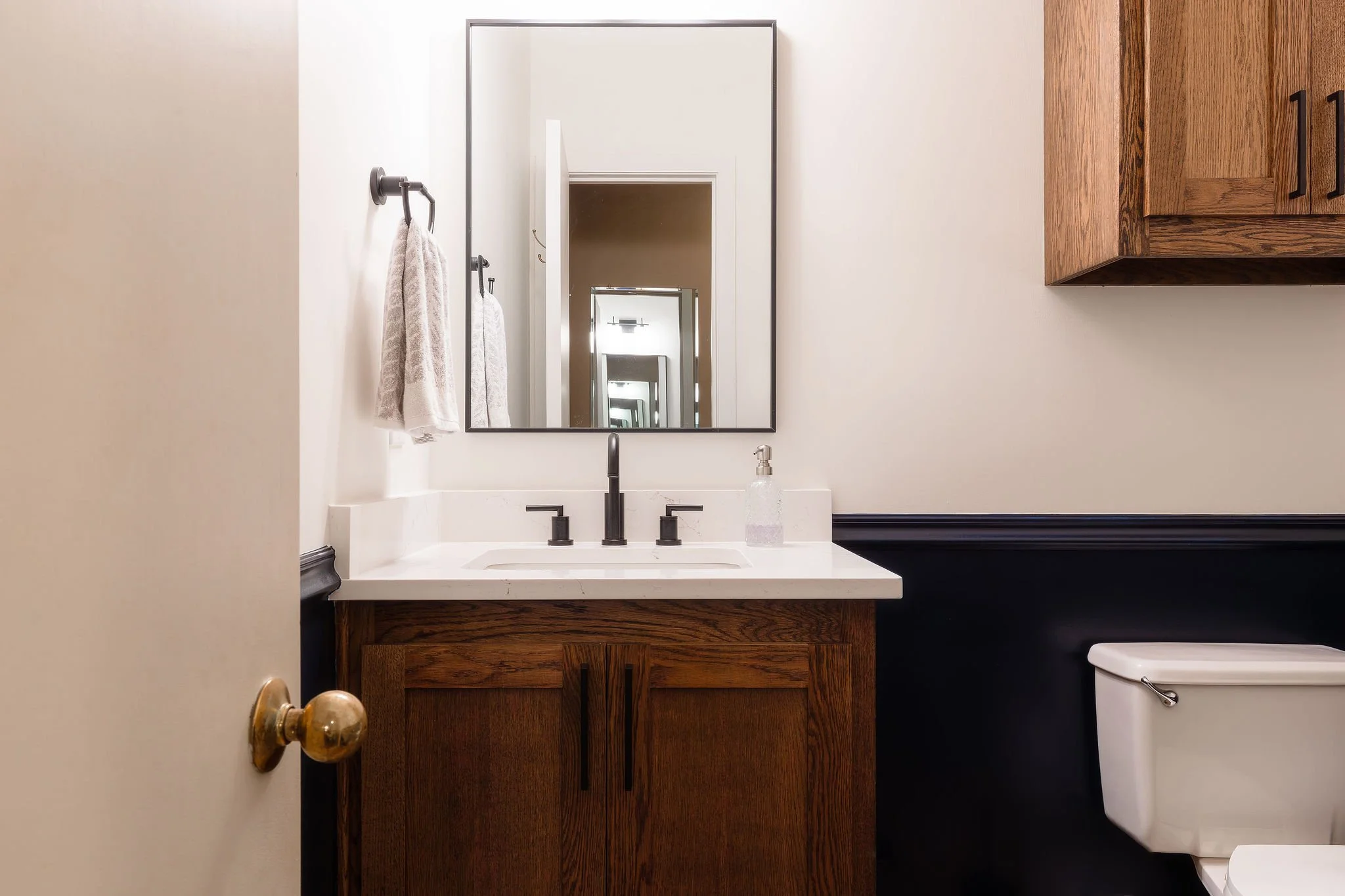 Close-up of a bathroom sink with a large mirror above it, a wooden cabinet below, and a towel hanging on a hook to the left.